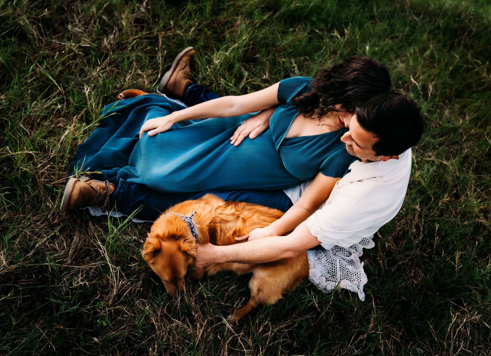 Maternity Photographer, pregnant woman in dress reclines in her husband, dog sits beside them in the grass