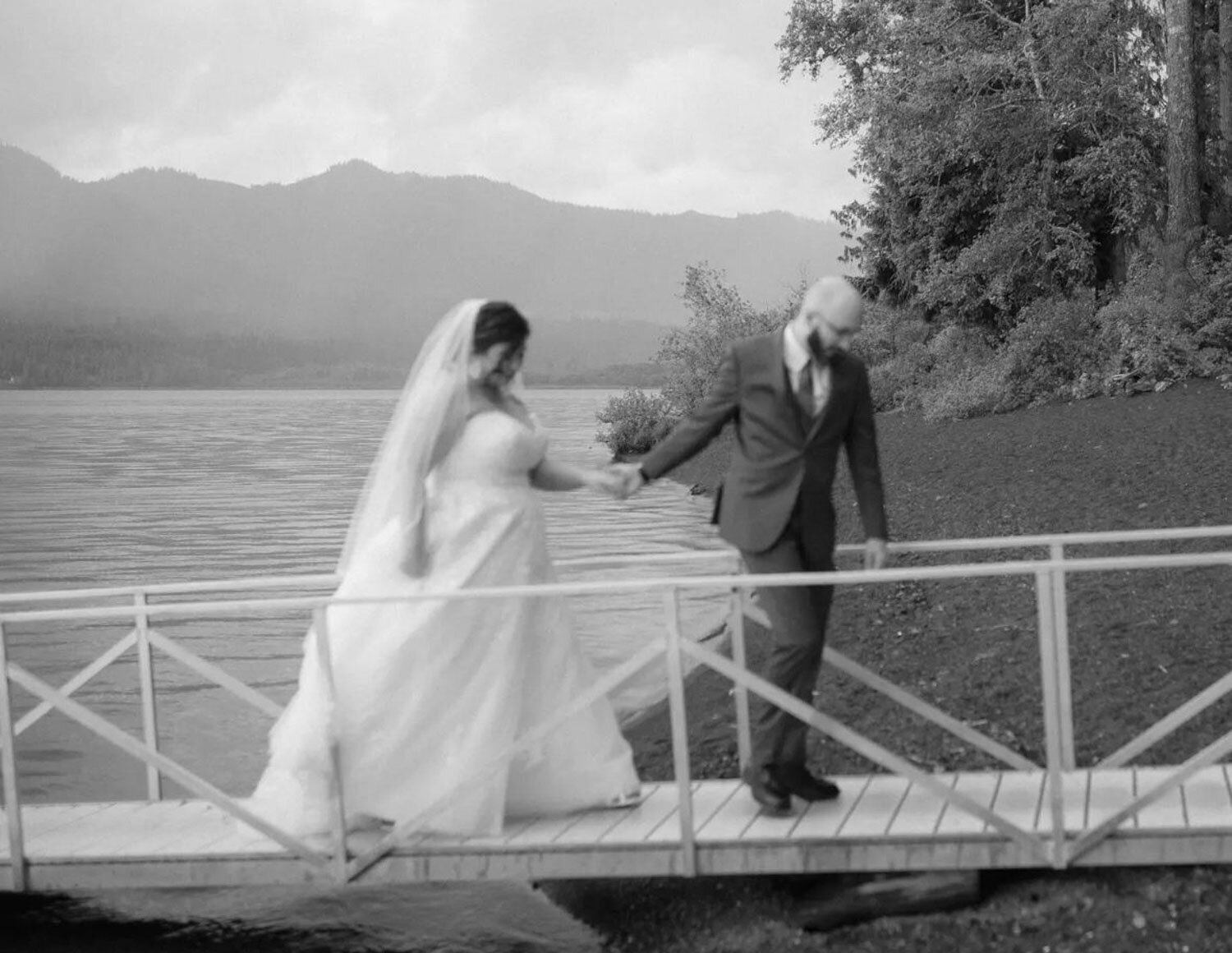 A bride and groom holding hands on a dock, captured in a timeless black-and-white shot