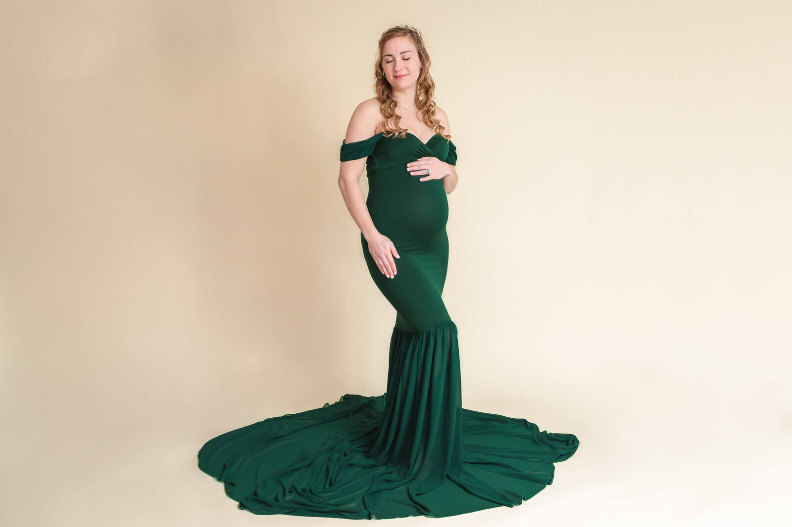 A woman in a green dress posing and holding her pregnant belly.
