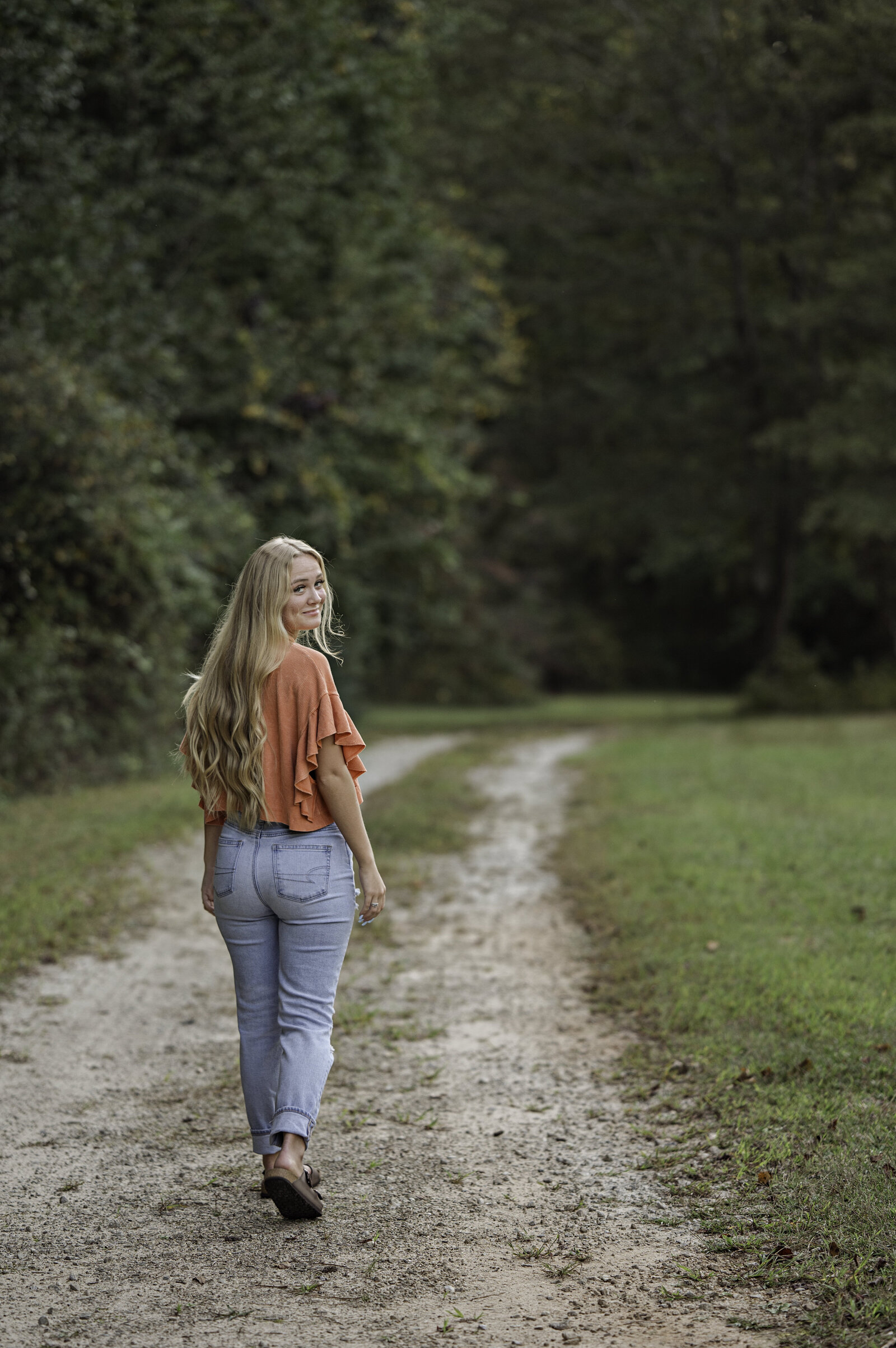 Beautiful blonde high school senior looks back as she walks down a gravel path