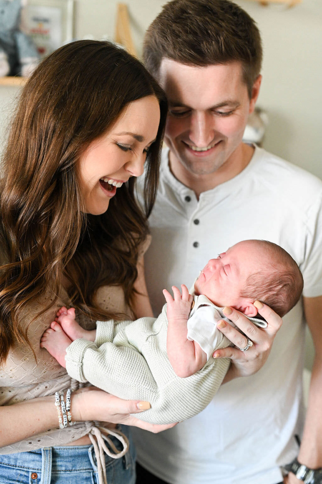 Parents holding out a newborn baby and smiling as they look down at them.