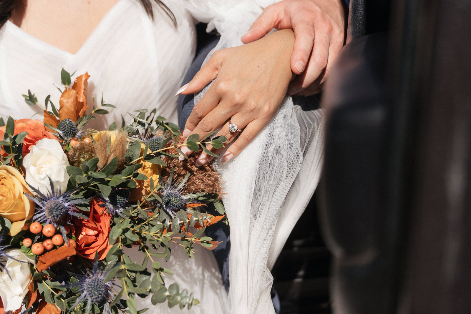 Close-up of bride’s hand with engagement ring resting on a colorful boho bouquet during a Sedona elopement at Merry-Go-Round Rock.