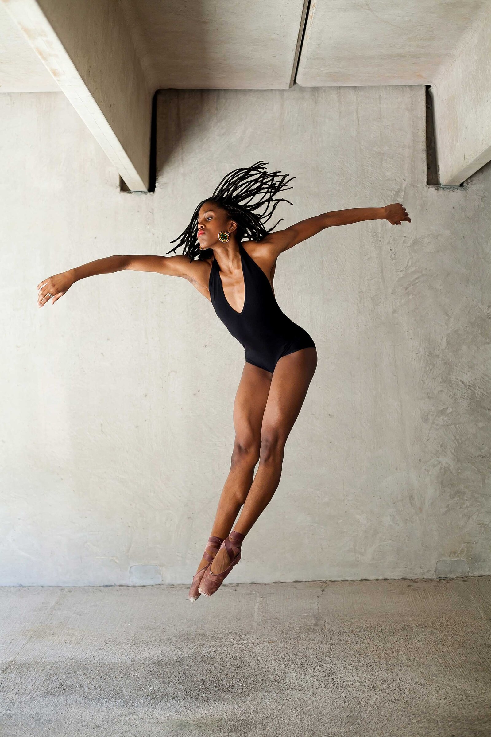 black woman ballerina in black leotard and brown pointe shoes and braids leaping