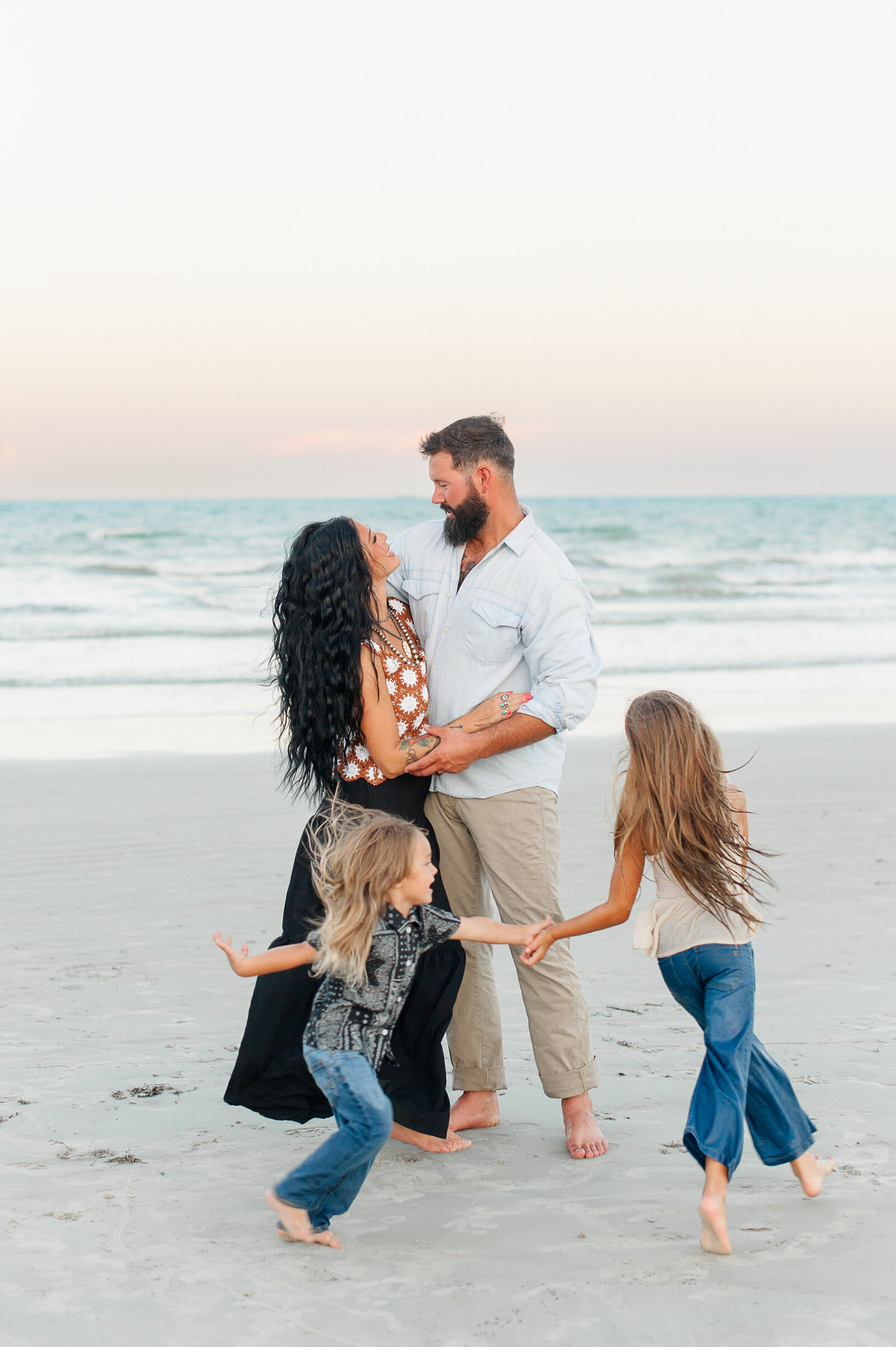 Children running on the beach around parents during family photos with Cocoa Beach photographer