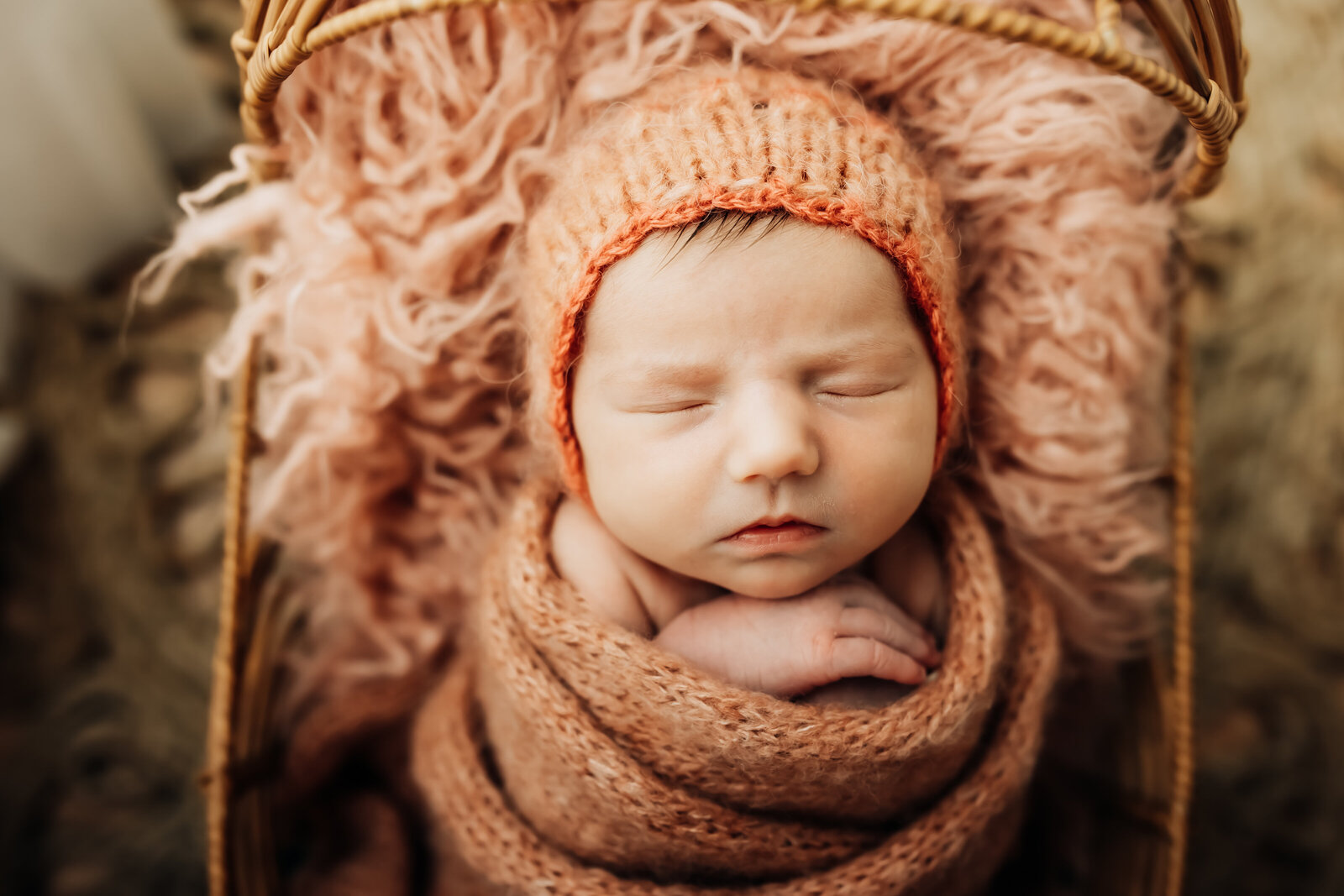Newborn baby girl in a warm pink bonnet and swaddle