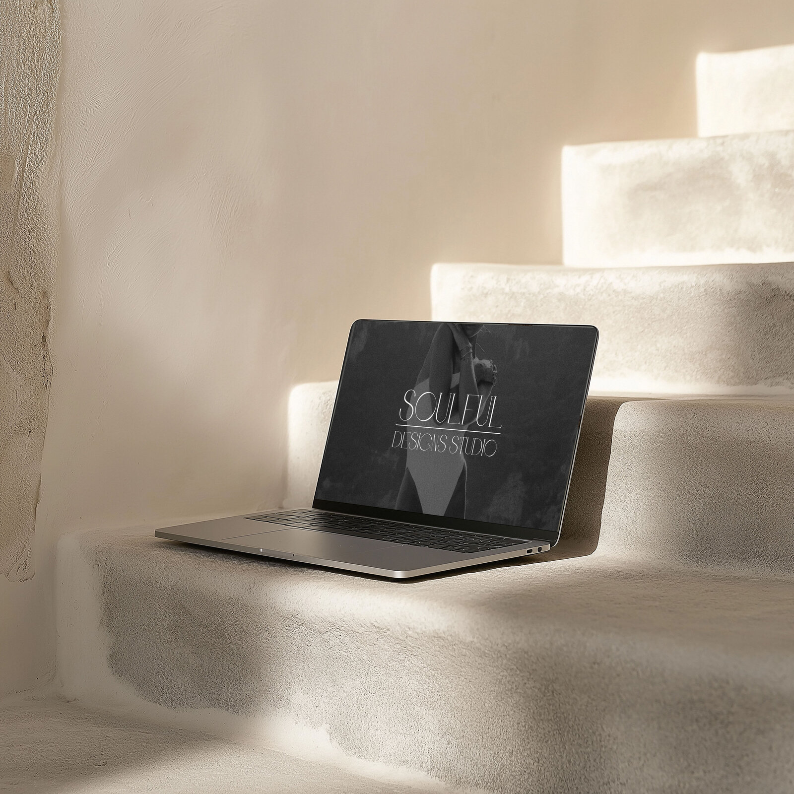 An opened laptop mockup on smooth beige stairs with a soulful designs studio brand wallpaper