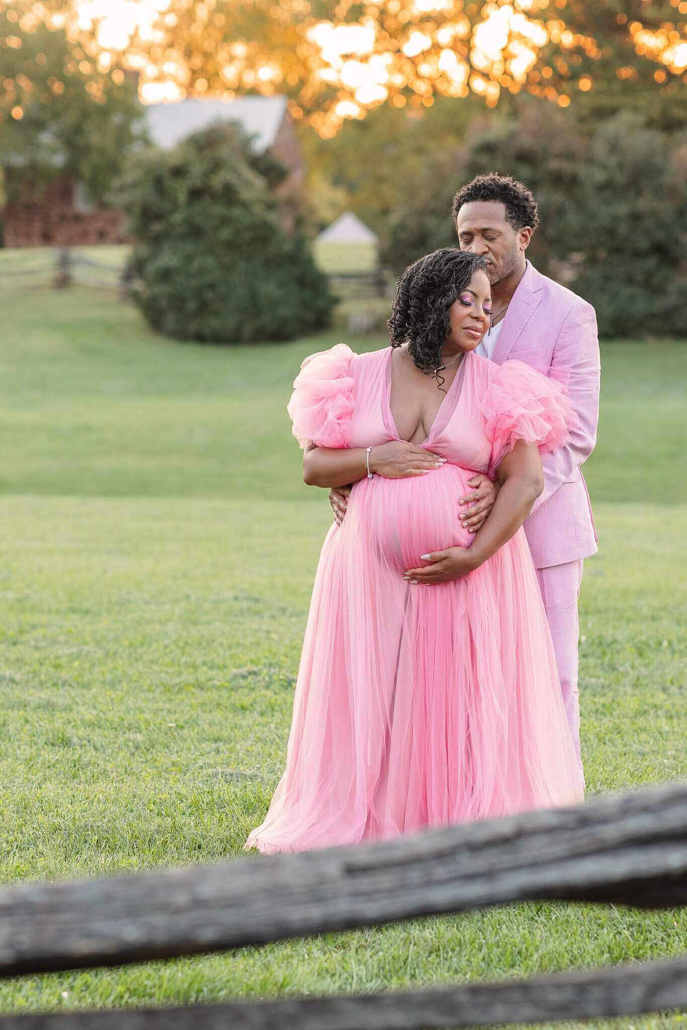 An expecting couple in pink snuggled up together at a park in Chantilly.