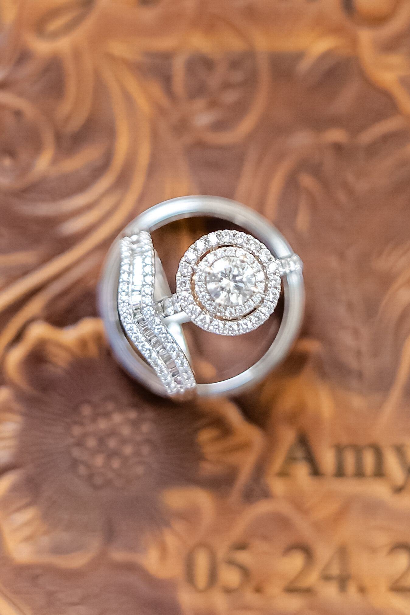 A close-up of diamond wedding rings displayed on an engraved wooden background with floral detailing, captured during a Outer Banks, NC wedding, showcasing elegant and personalized wedding details.