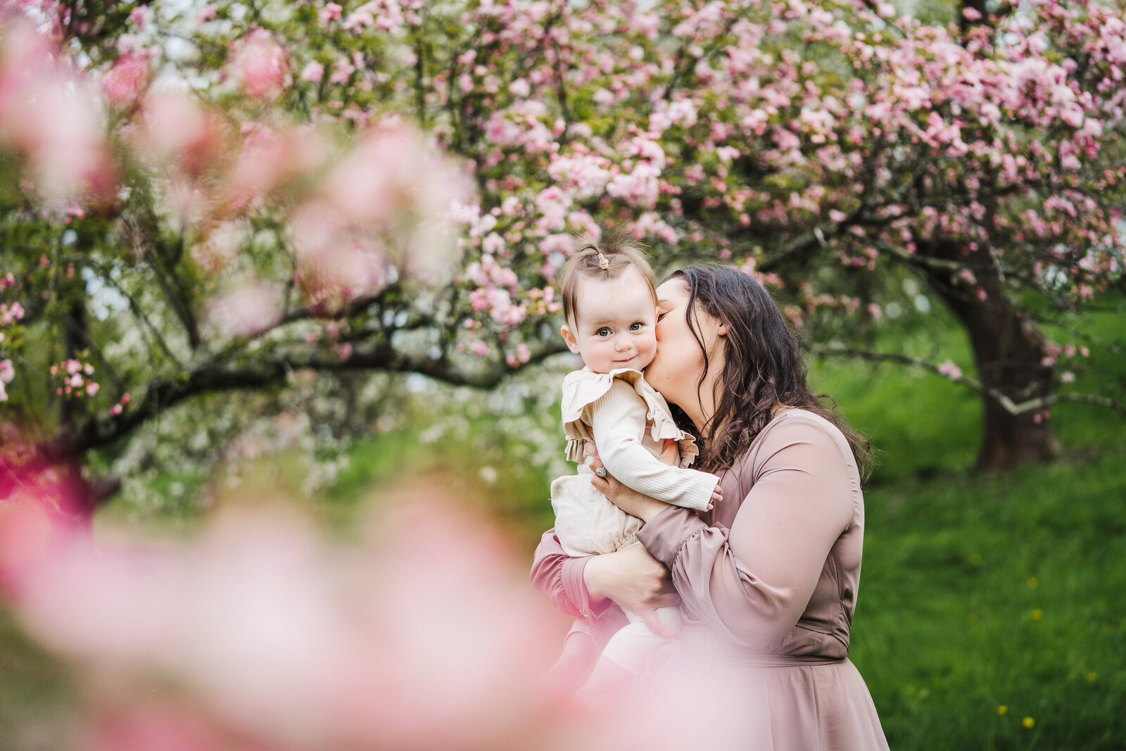 mom kisses daughter among pink blossoming trees
