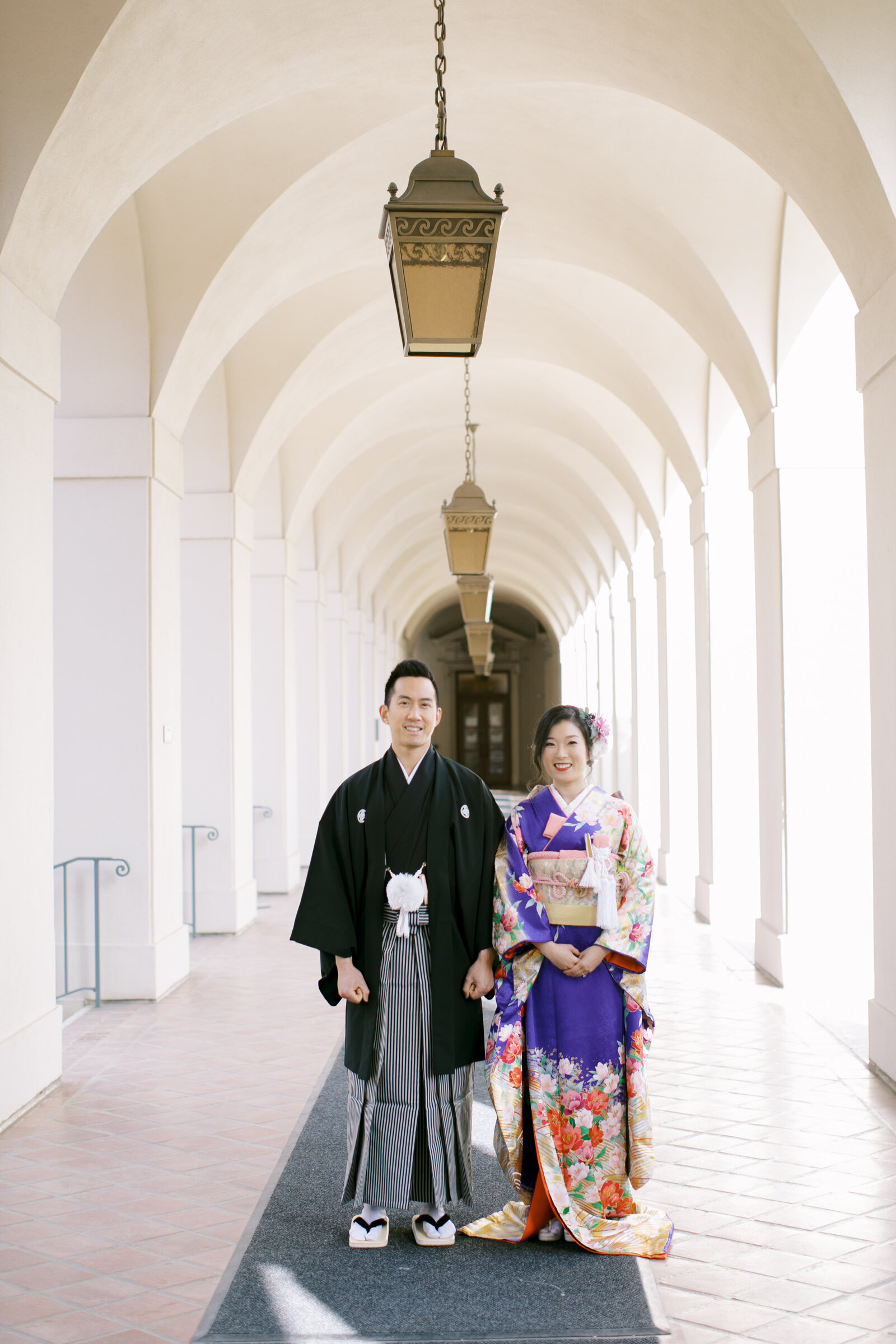 Bride in vibrant purple wedding kimono rental and groom in black montsuki standing under the elegant archway of Pasadena City Hall, California | パサデナ市庁舎 アーチ下で着物レンタルウェディング 新郎新婦