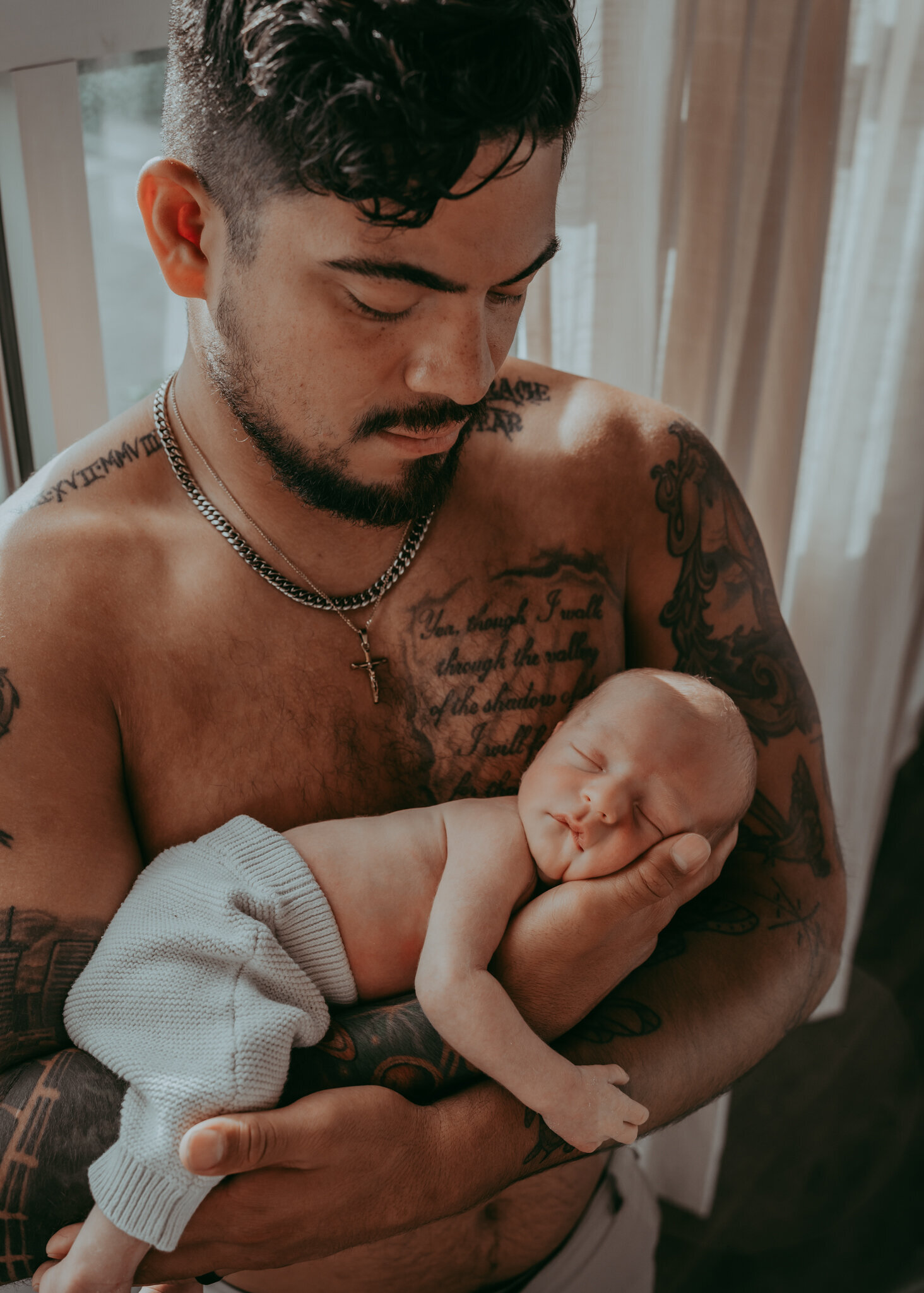 shirtless tattooed dad holds sleeping baby boy