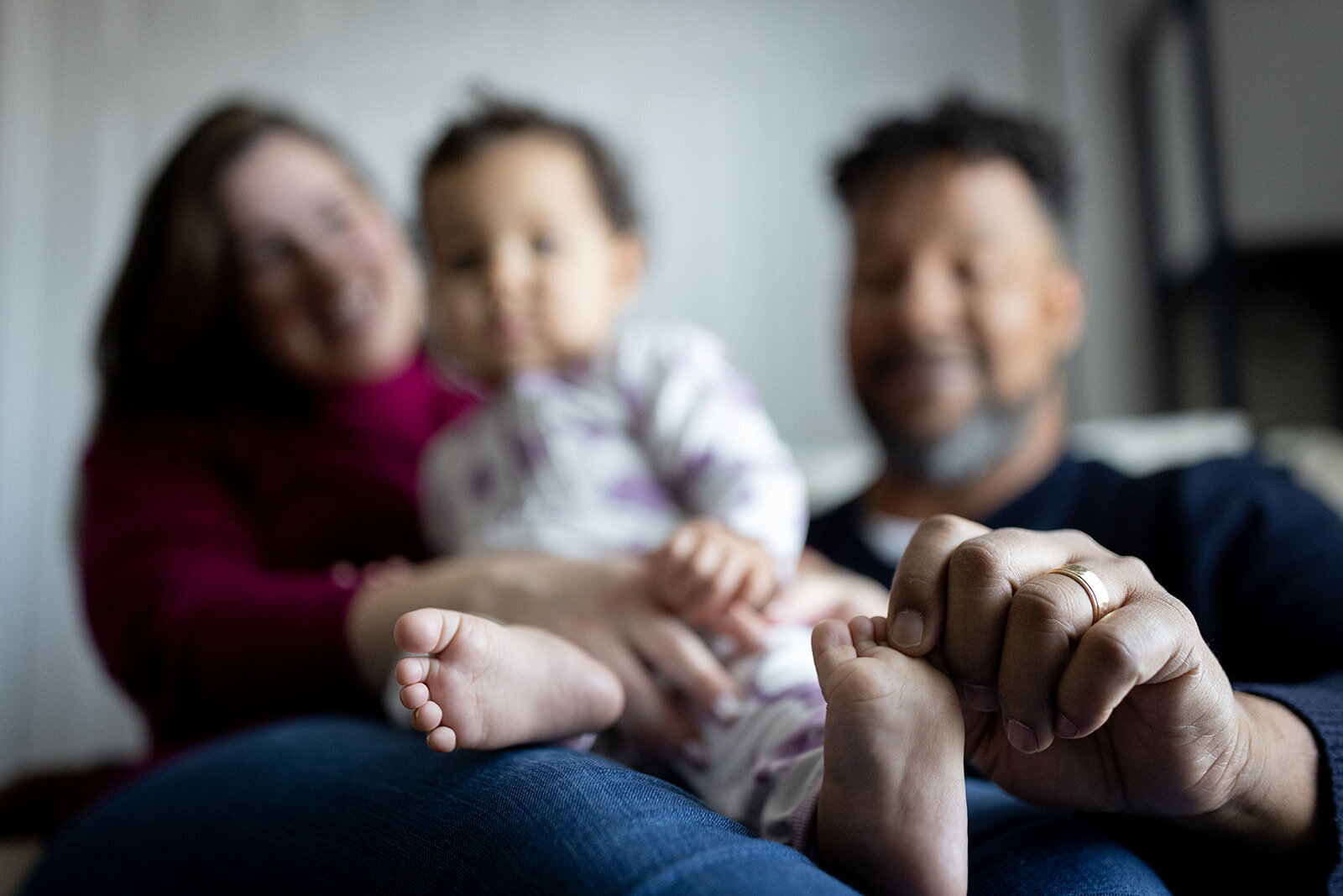 "A heartfelt close-up of a family, focusing on a baby’s tiny feet held gently by the father, with the parents smiling warmly in the background."