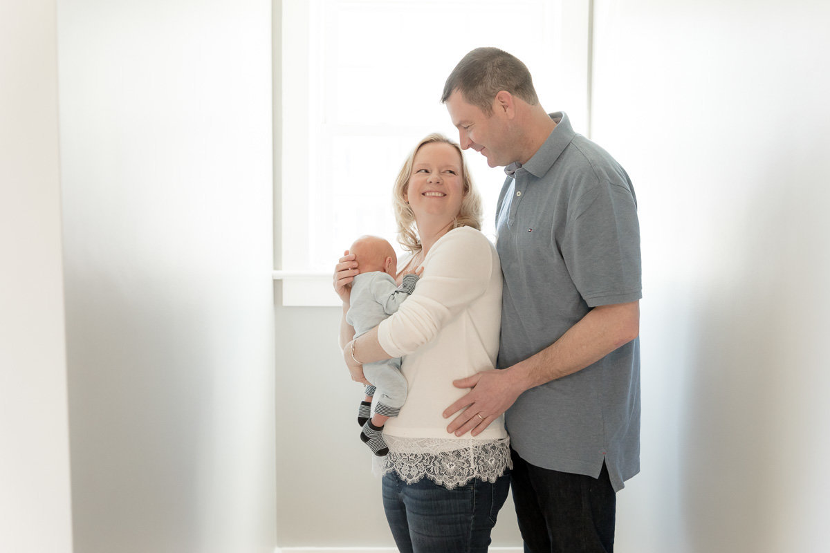 new parents stand close and smile over newborn's head