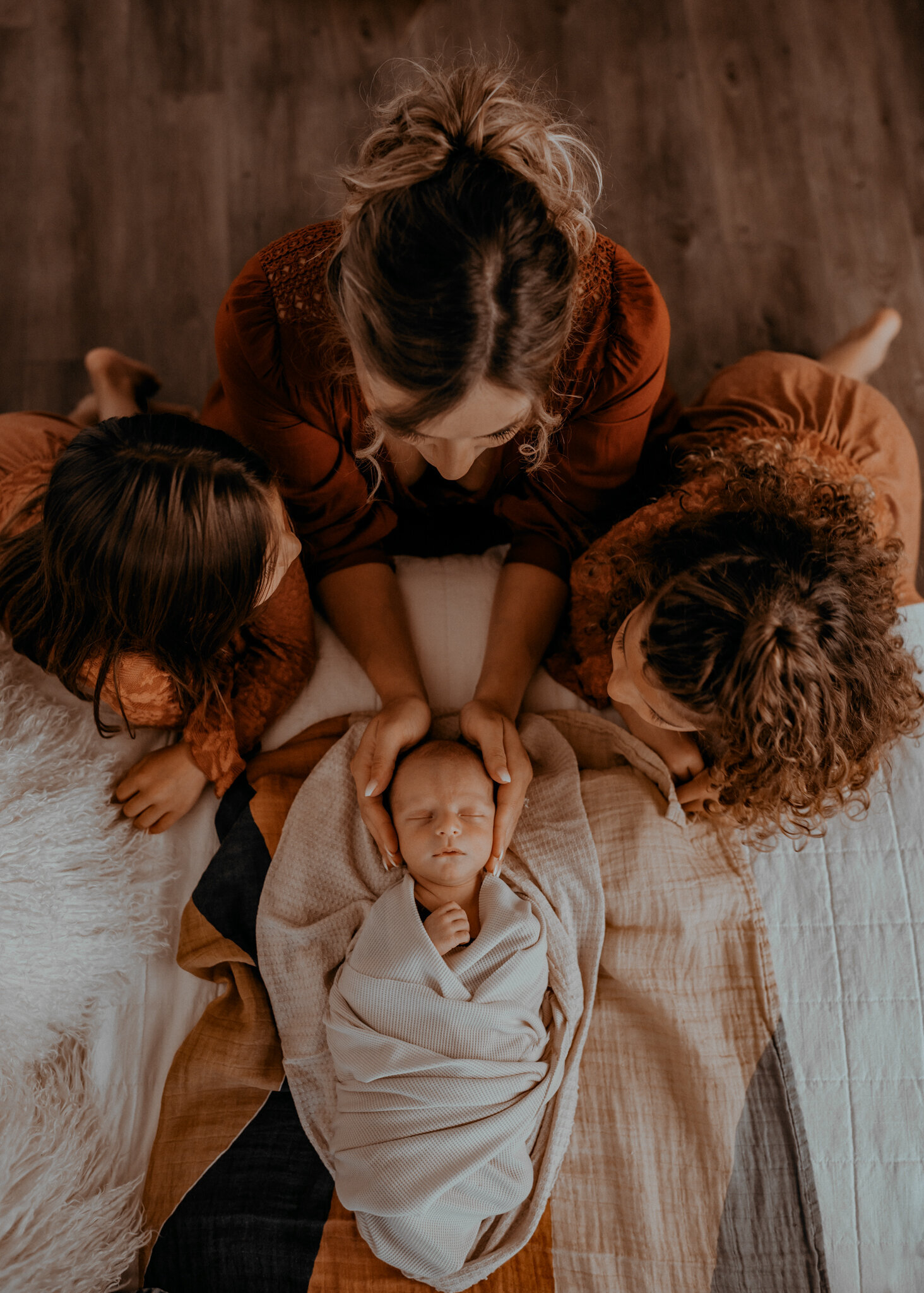 mother holds infant's head while big sisters gather around