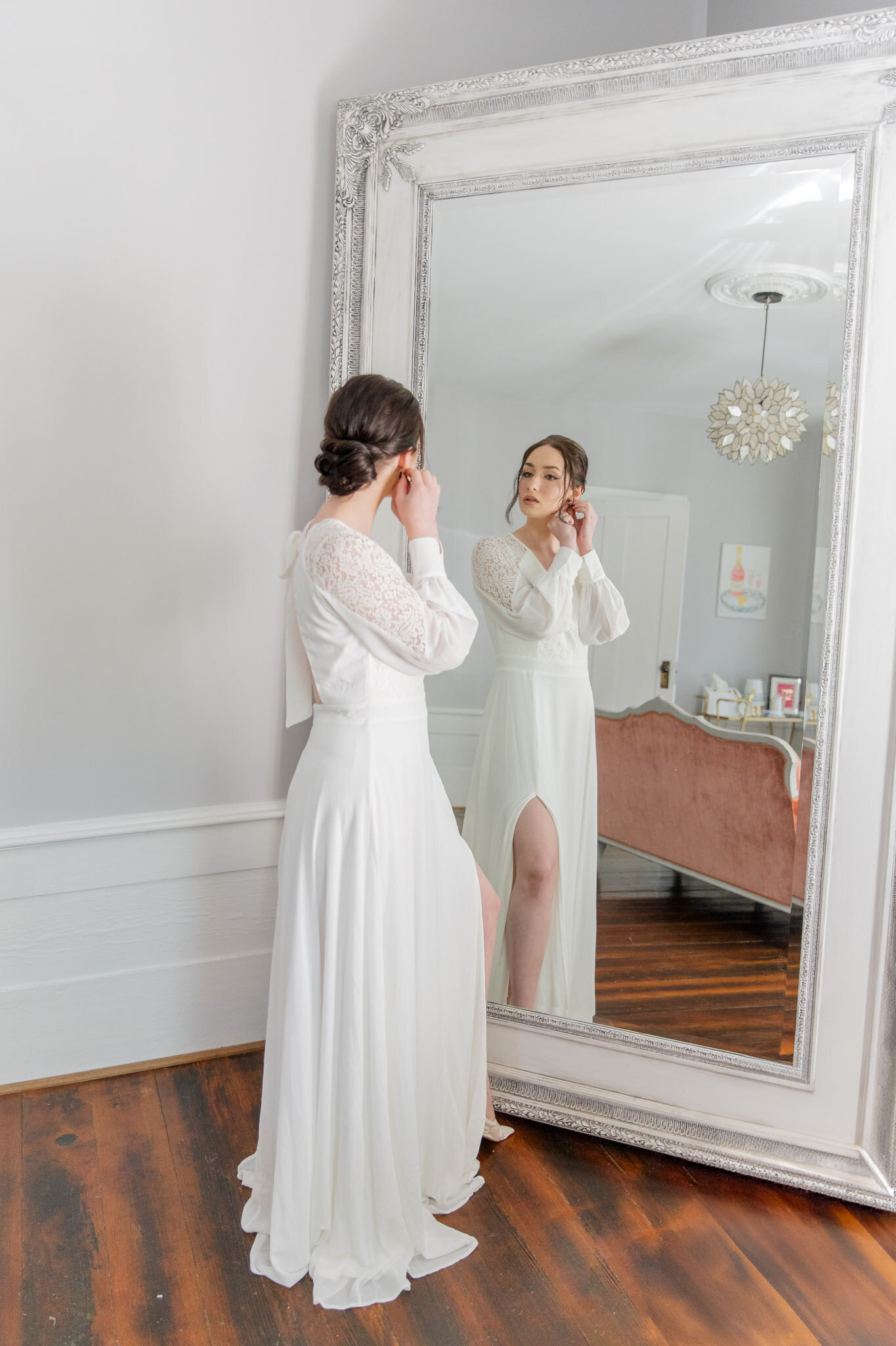 A woman gets ready for her elopements. She's wearing a simple white dress and putting in her earrings.