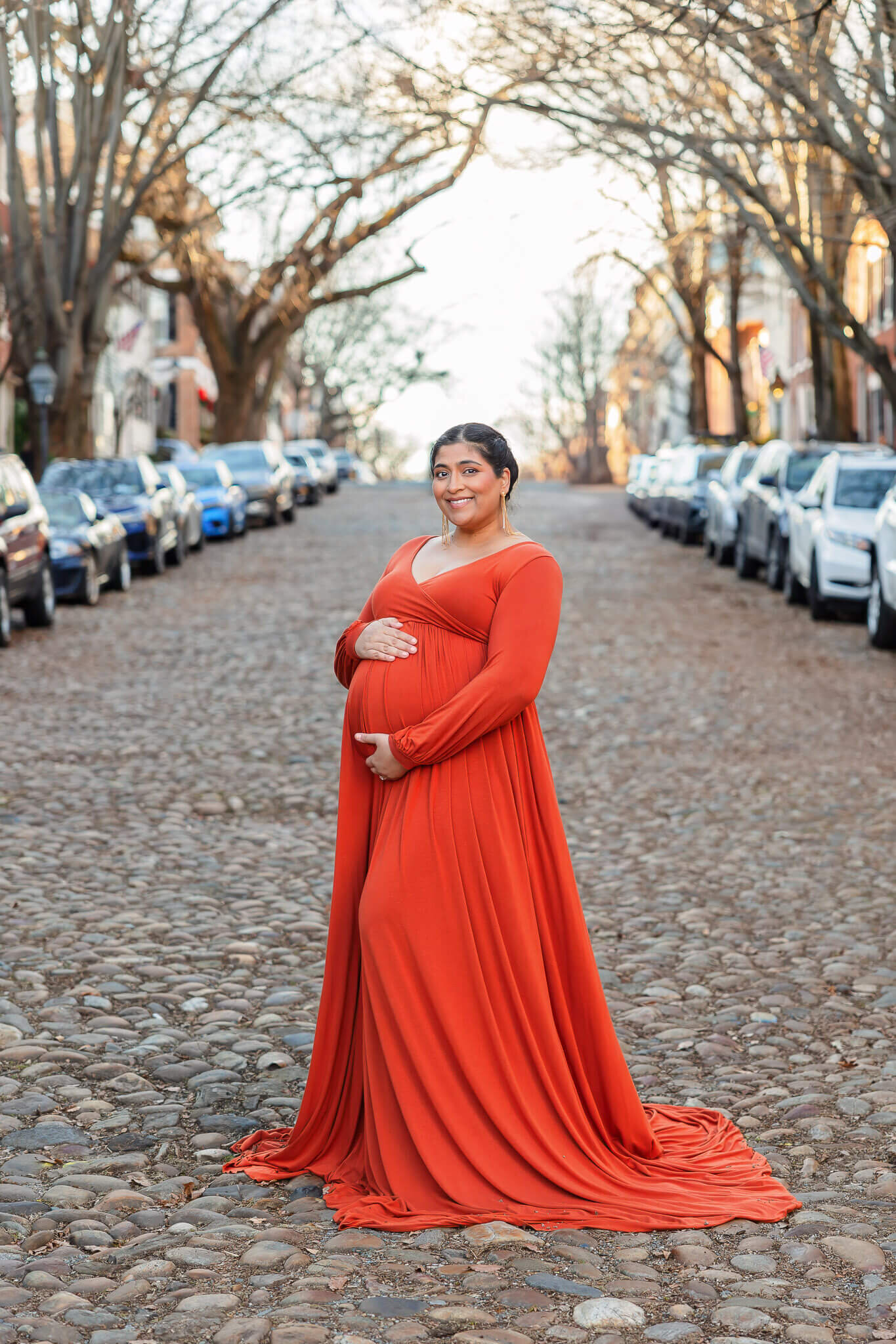 A mom-to-be in an orange dress on a cobblestone street.