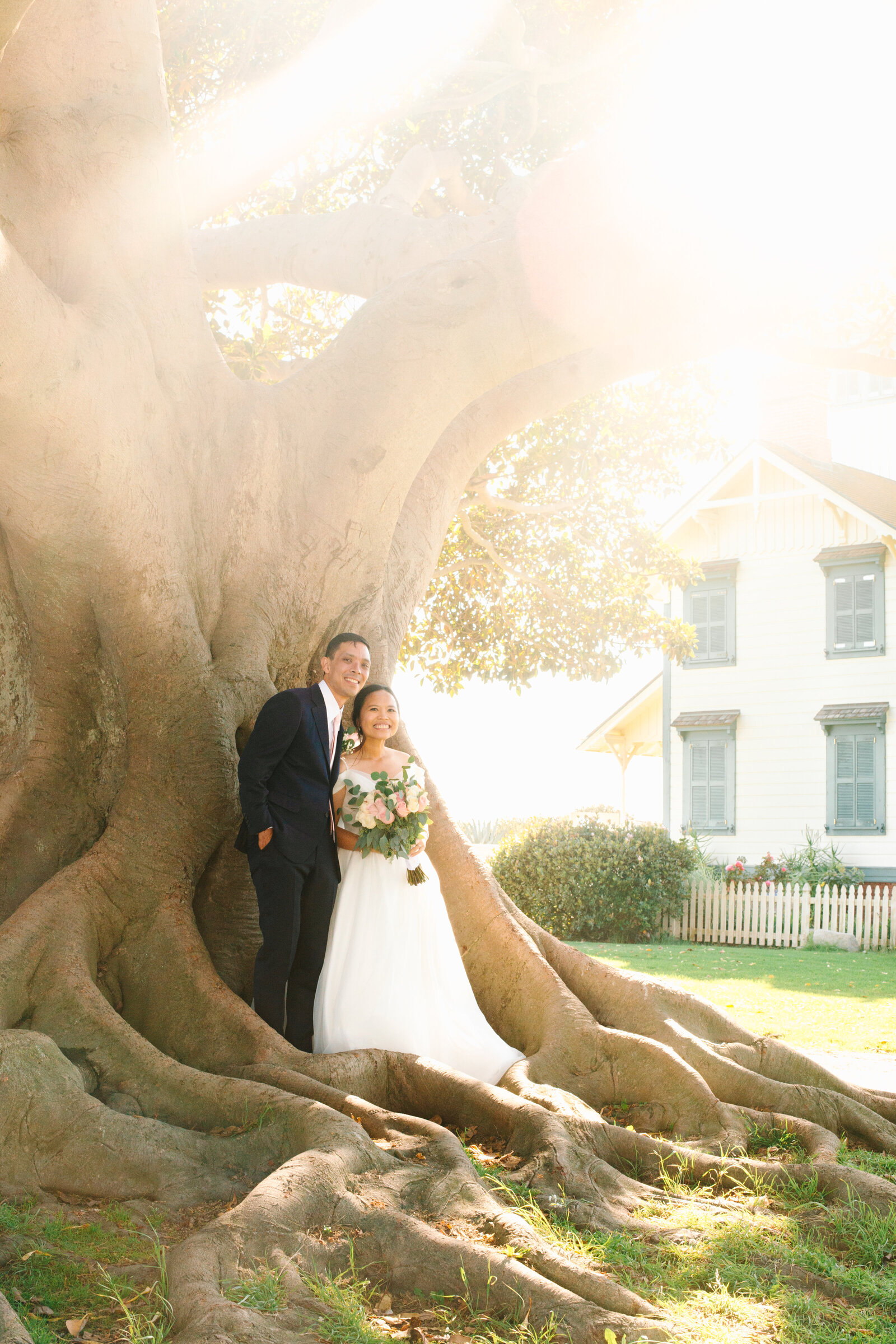 A bride and groom stand underneath a large tree on a sunny Los Angeles day.