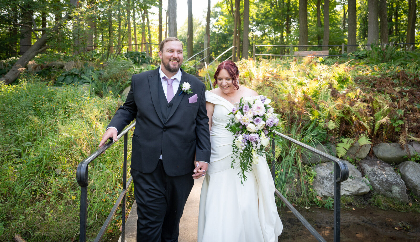 wedding couple walk hand in hand along small bridge