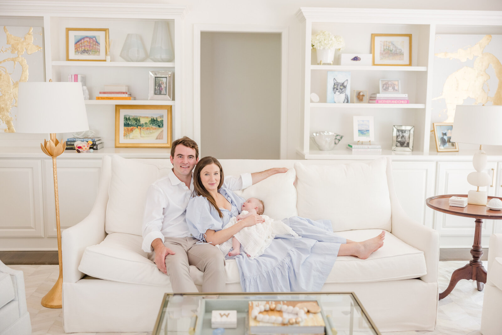 Parents smiling for photos while seated on a couch holding their newborn.