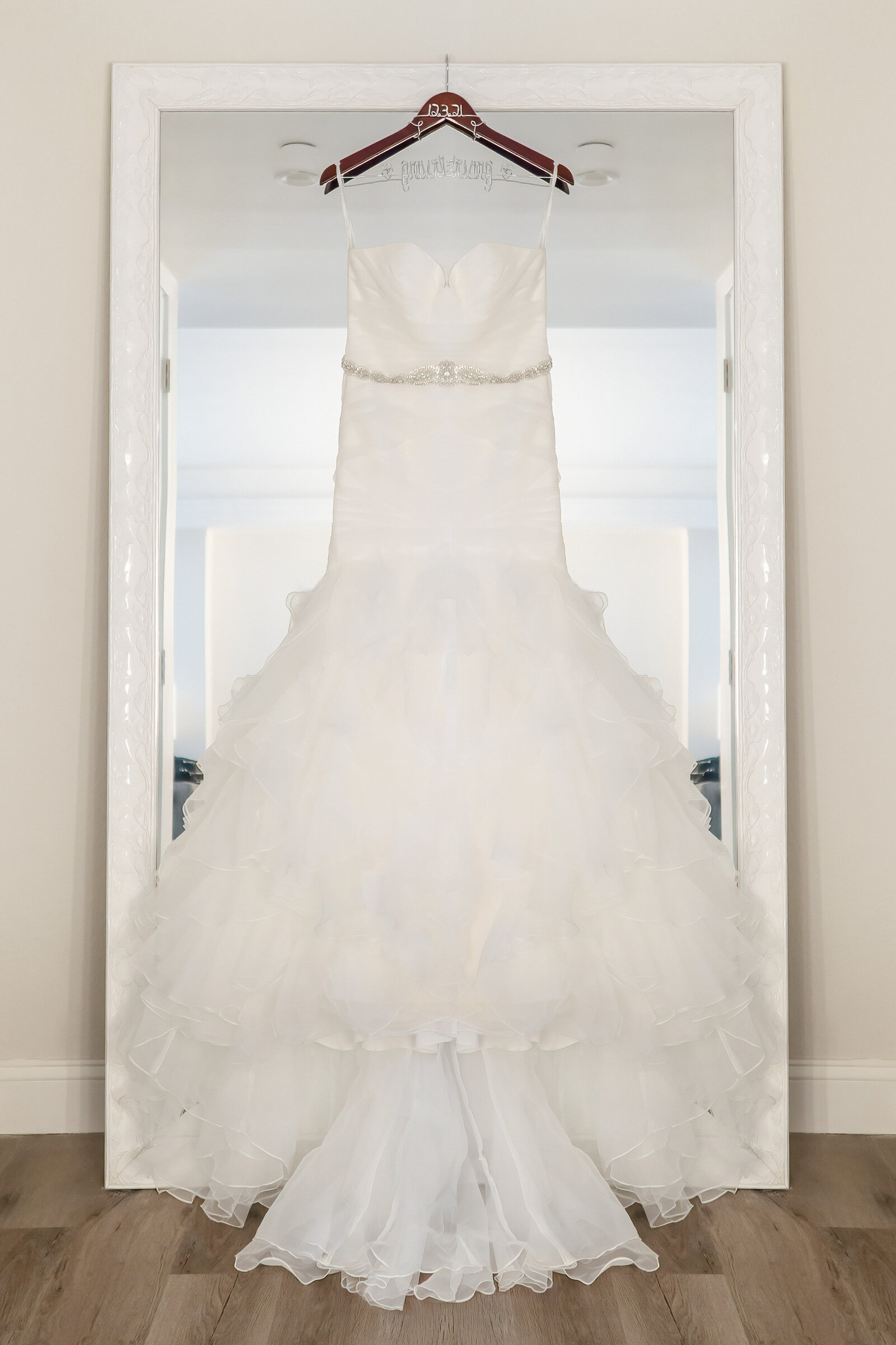 Elegant wedding dress displayed in front of a large mirror, capturing the intricate details and beauty in preparation for the special day in Wilmington, NC.