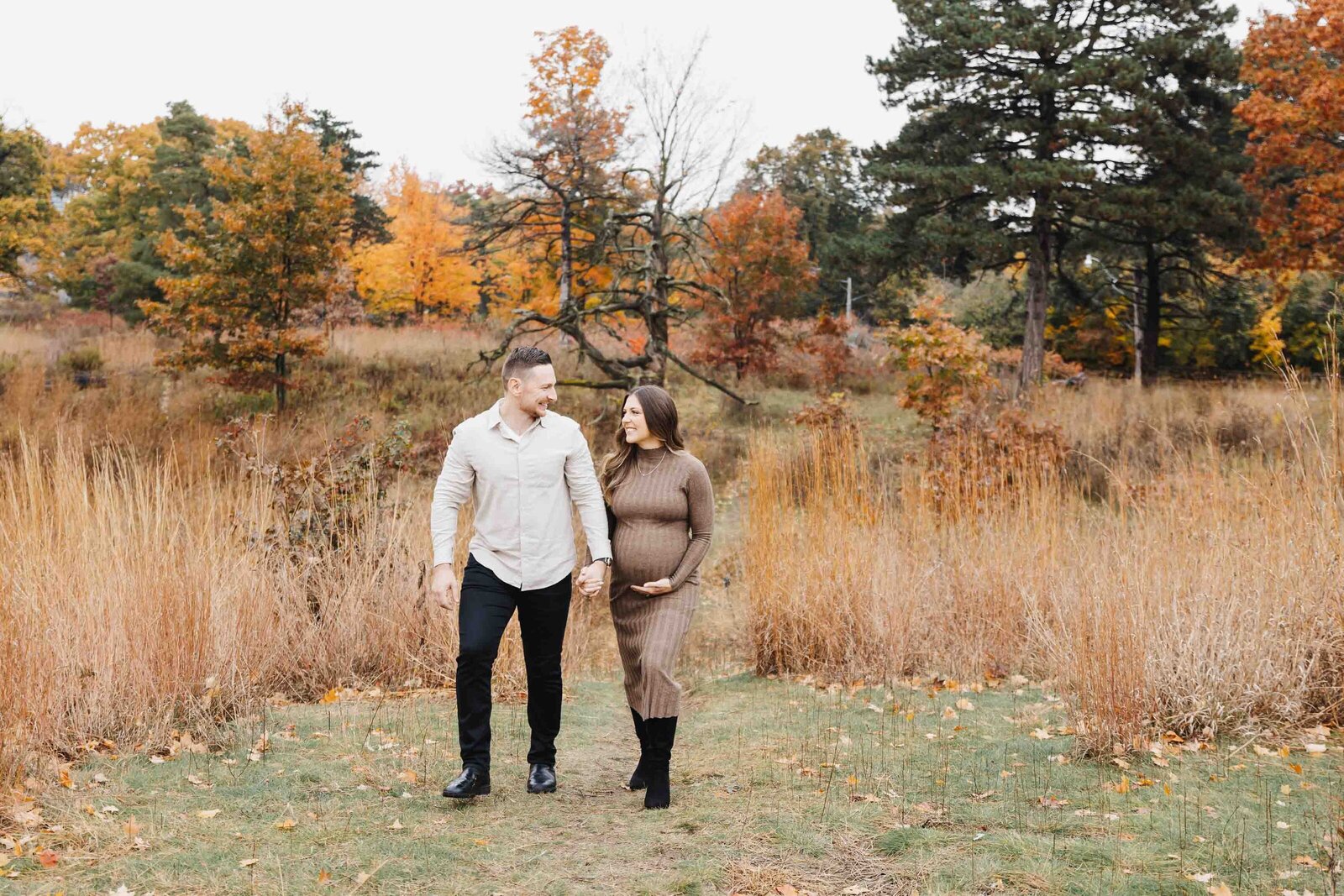 Pregnant women in fitted brown knit dress holding hands with her husband and walking