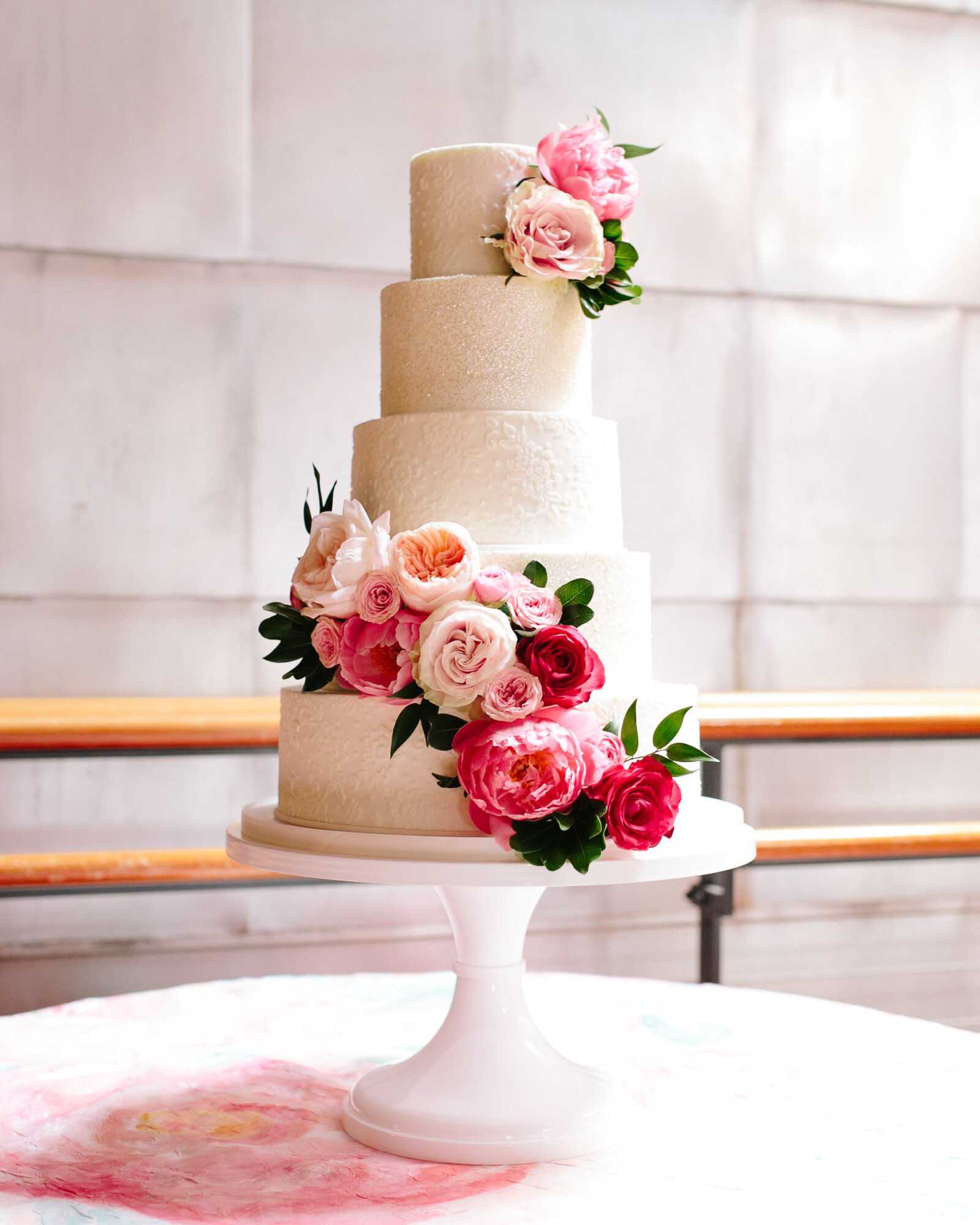 Feminine stylish white buttercream wedding cake with lace pattern glitter tiers  and color vibrant flower blooms and greenery at Bay 7 Durham McLean Events