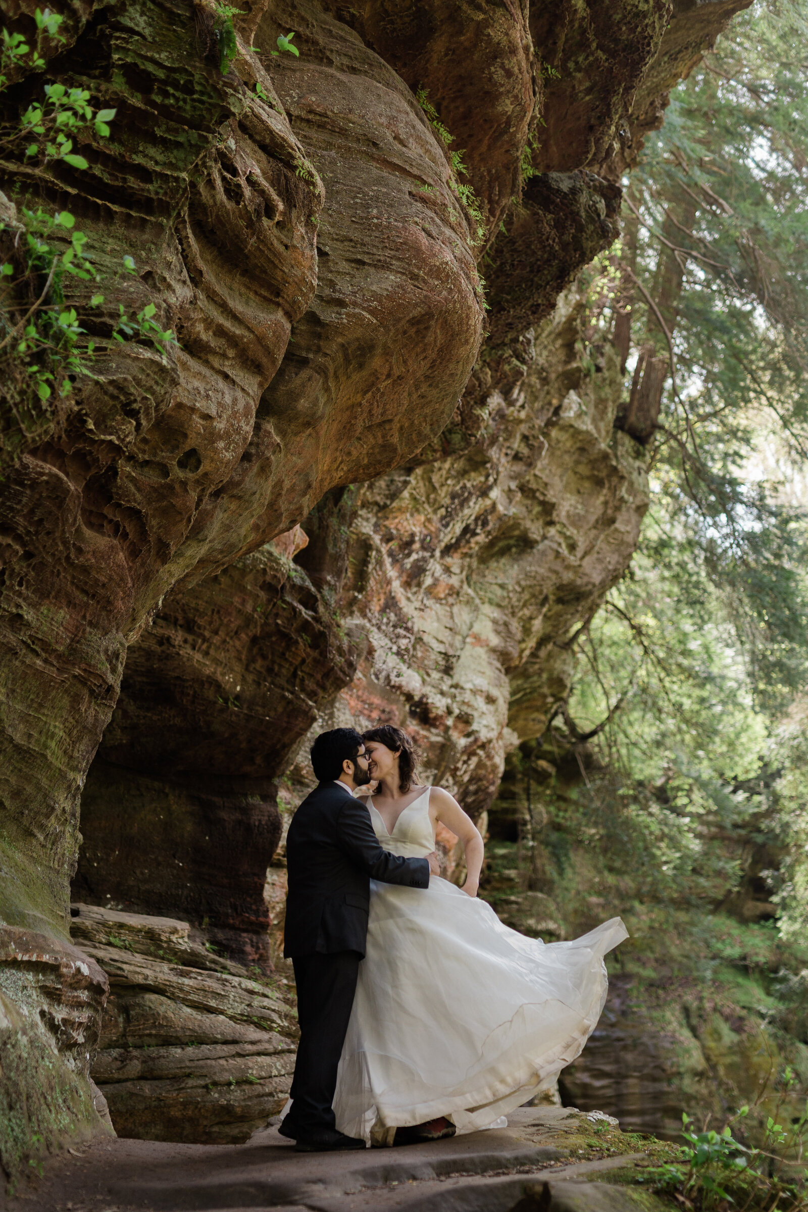 Interracial couple stand close to each other with a cave scenery background