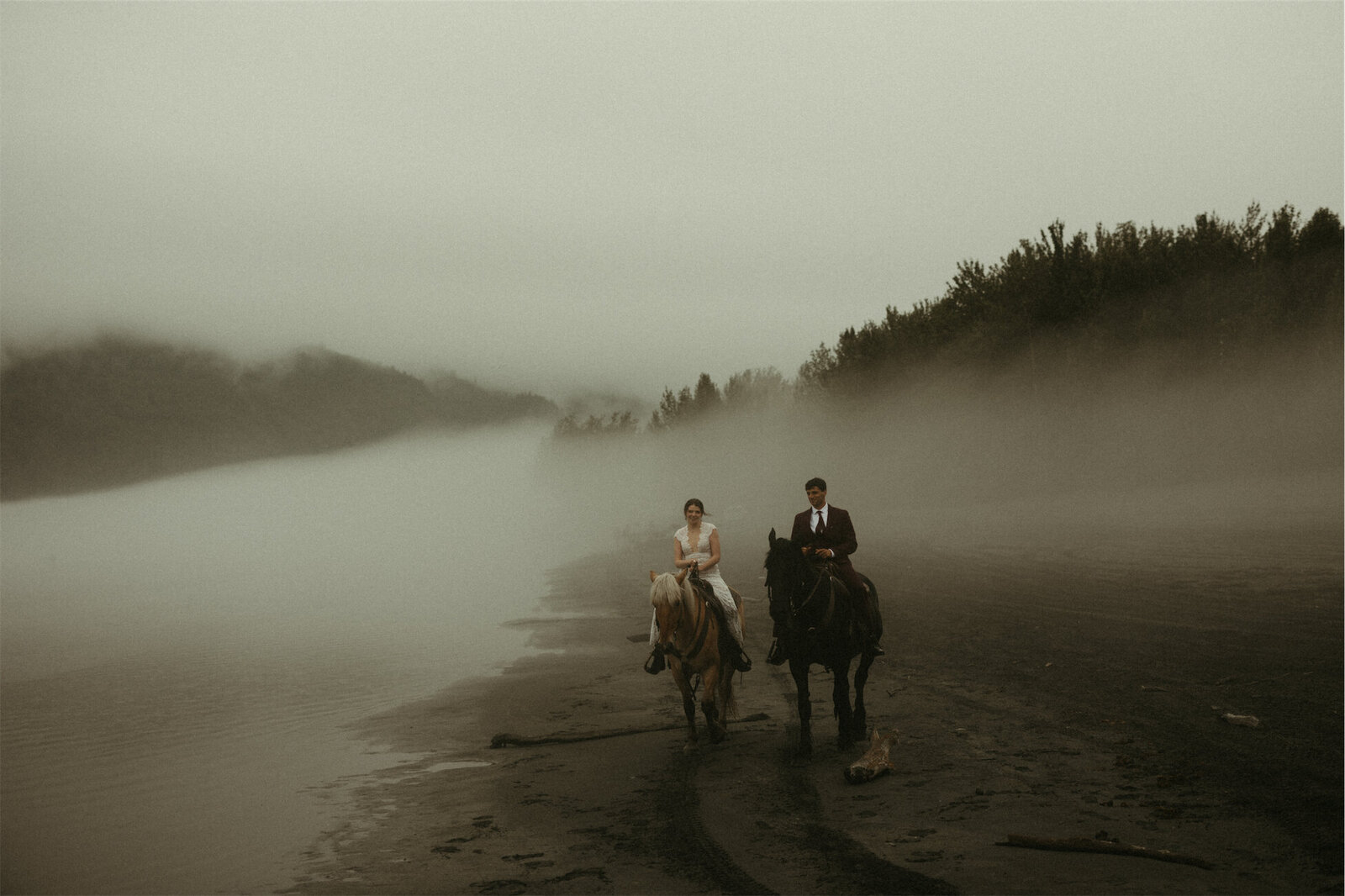 Couple in wedding attire walking across a foggy beach in Palmer, Alaska