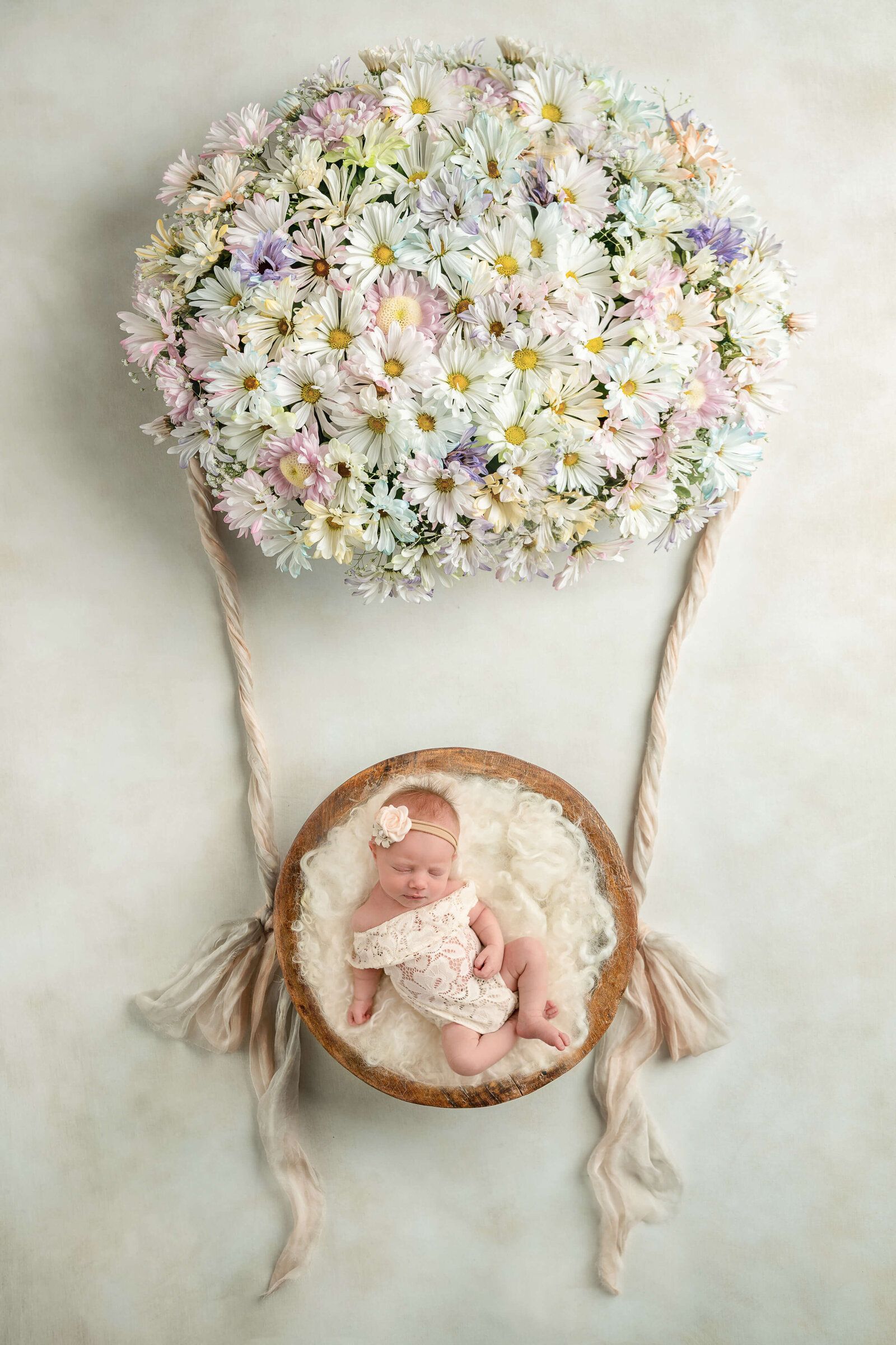 Newborn in lace outfit sleeping in a hot air balloon with a flower headband at Jen Sabatini Photography