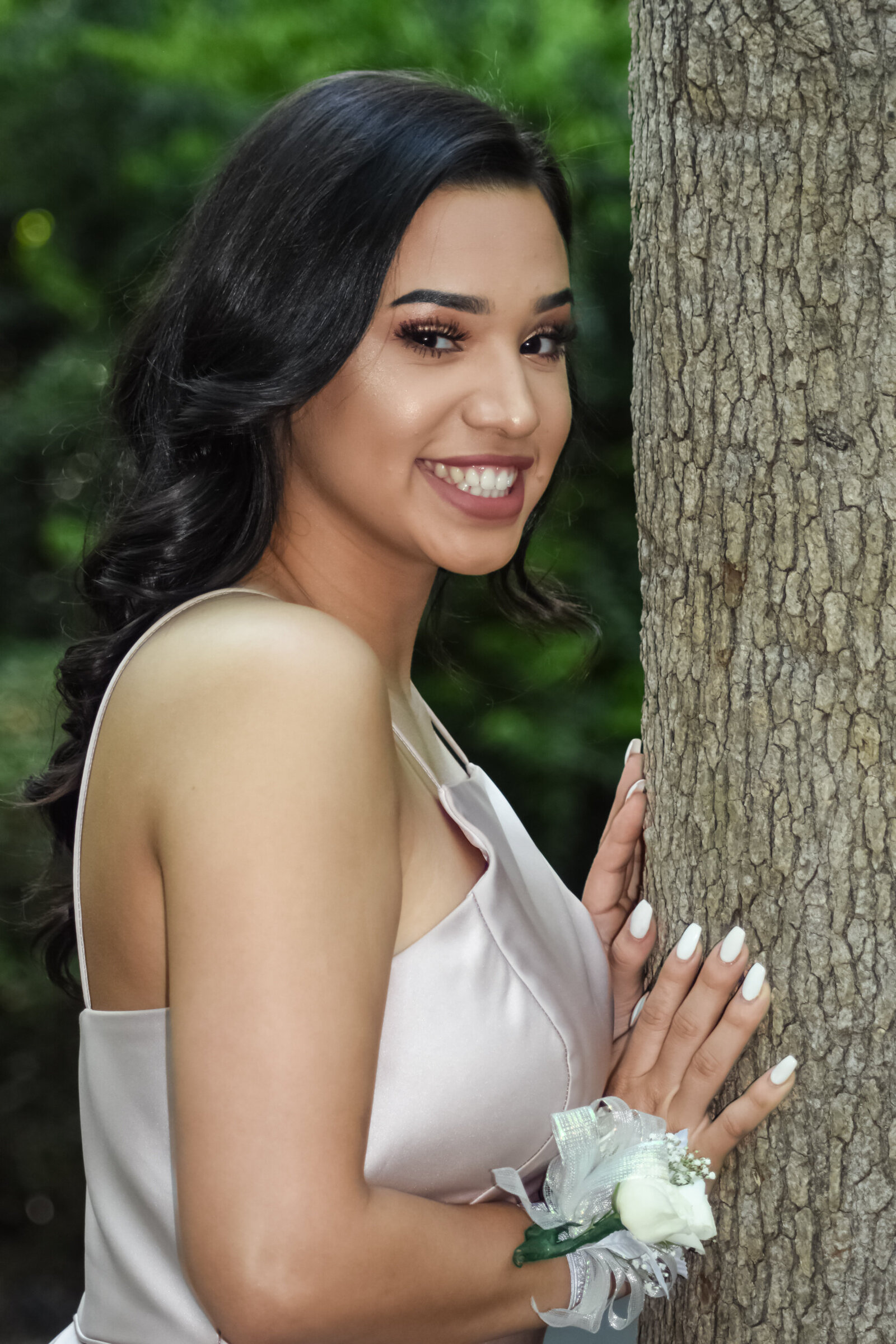 a young woman in her prom dress wearing a white corsage posing against a tree. photographed by Millz Photography in Greenville, SC