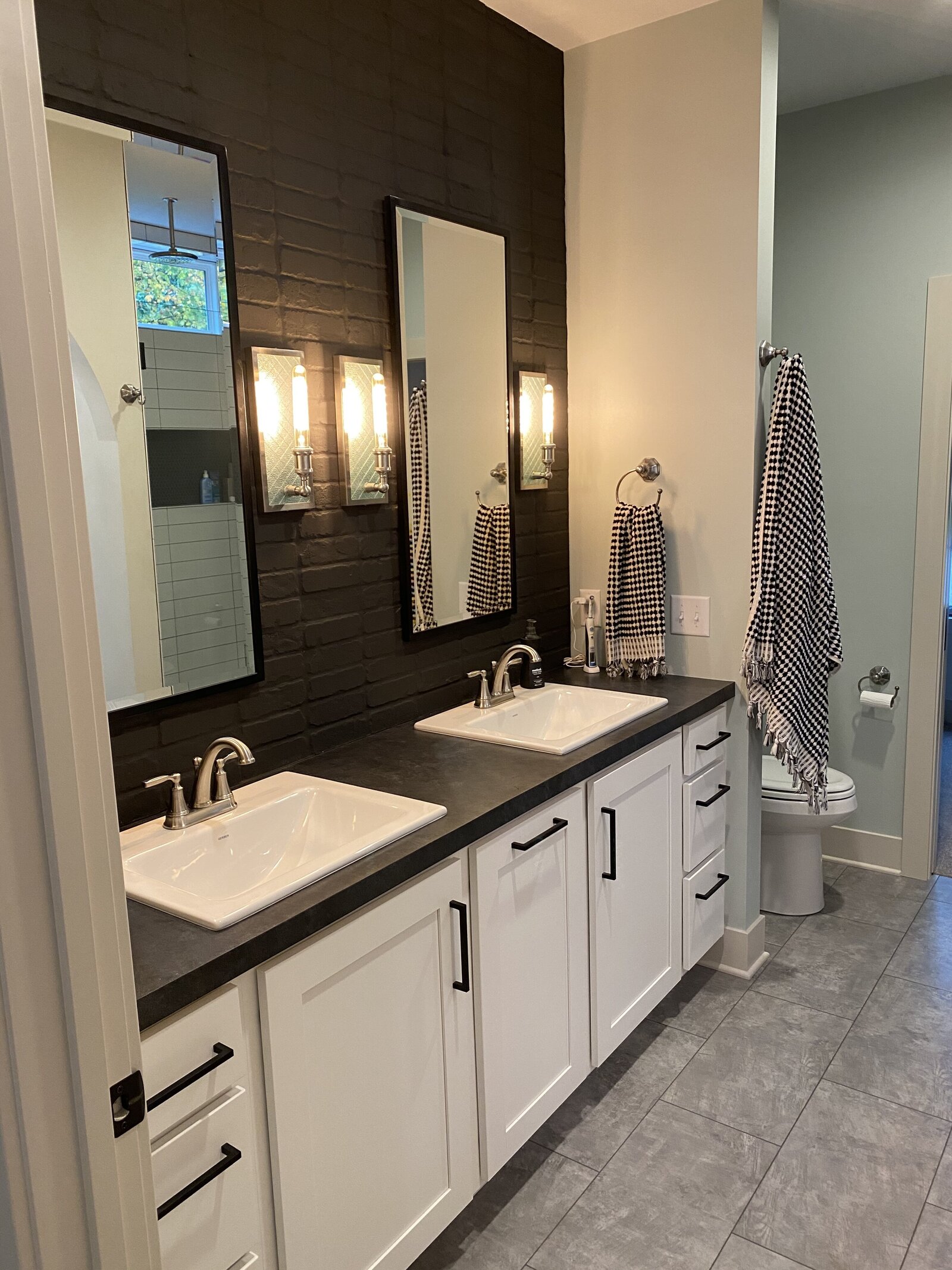 Bathroom view with white cabinetry, black countertops and black brick backsplash.
