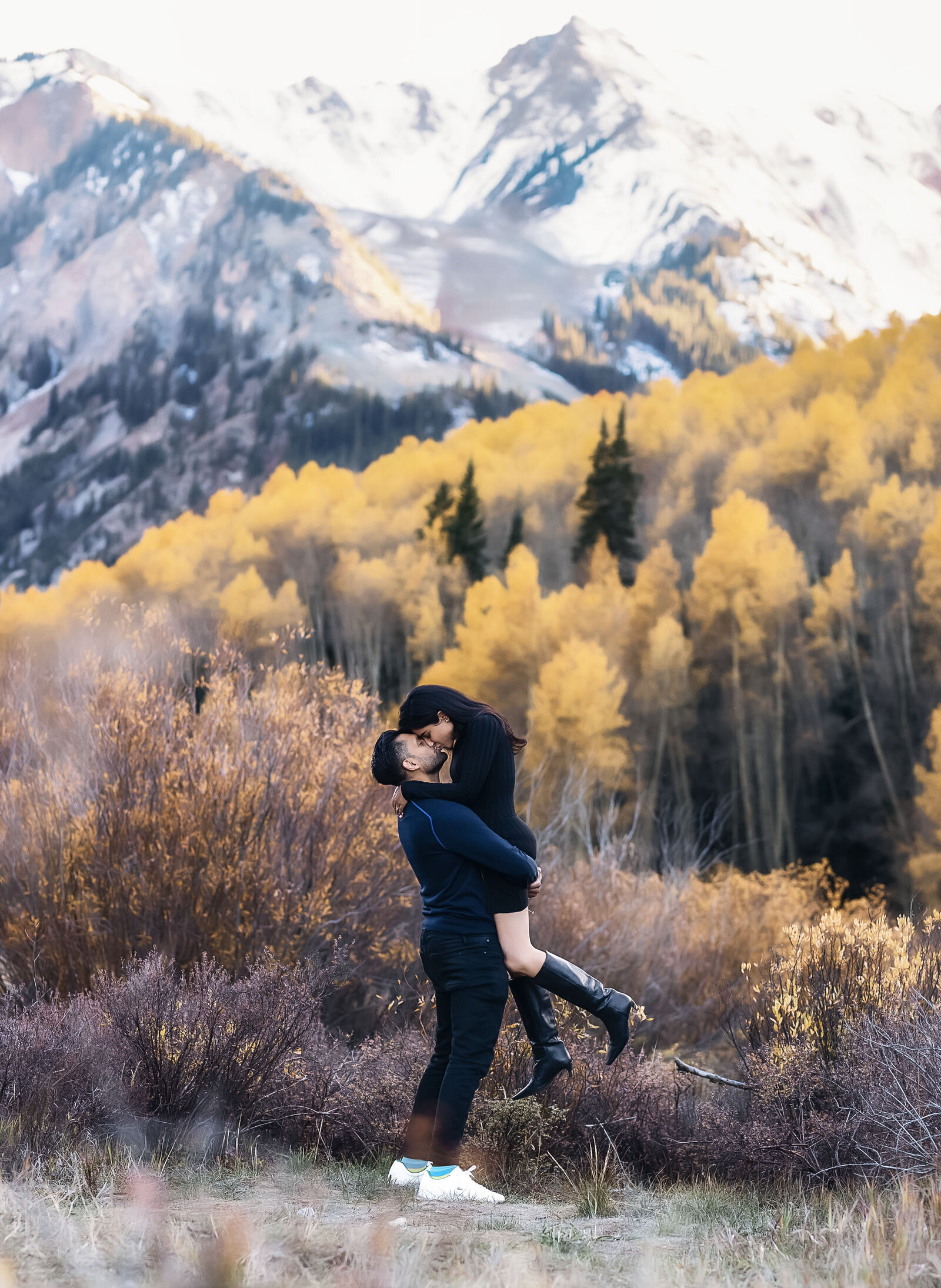 A man lifts his beautiful fiance up  as they celebrate their Aspen mountain proposal.