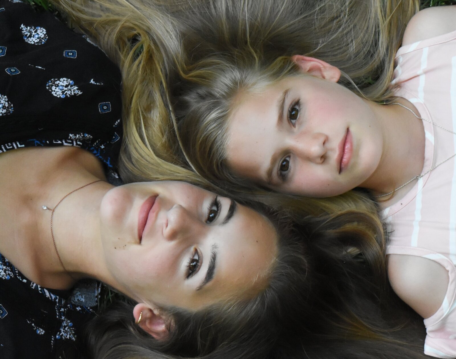two girls laying on the ground with their heads touching while they look up at the camera photographed by Millz Photography in Greenville, SC