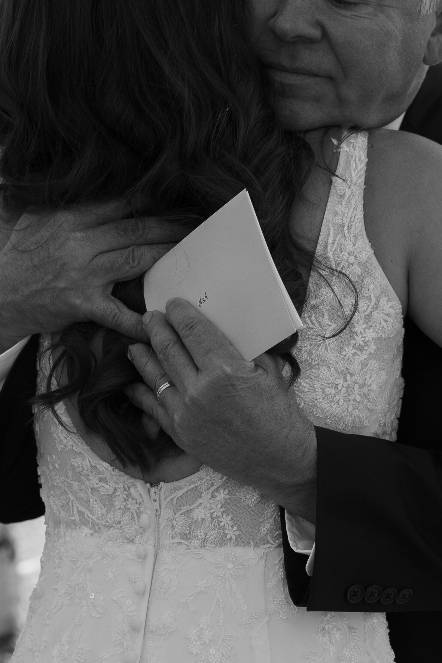 dad holding card from bride while hugging her during their first look