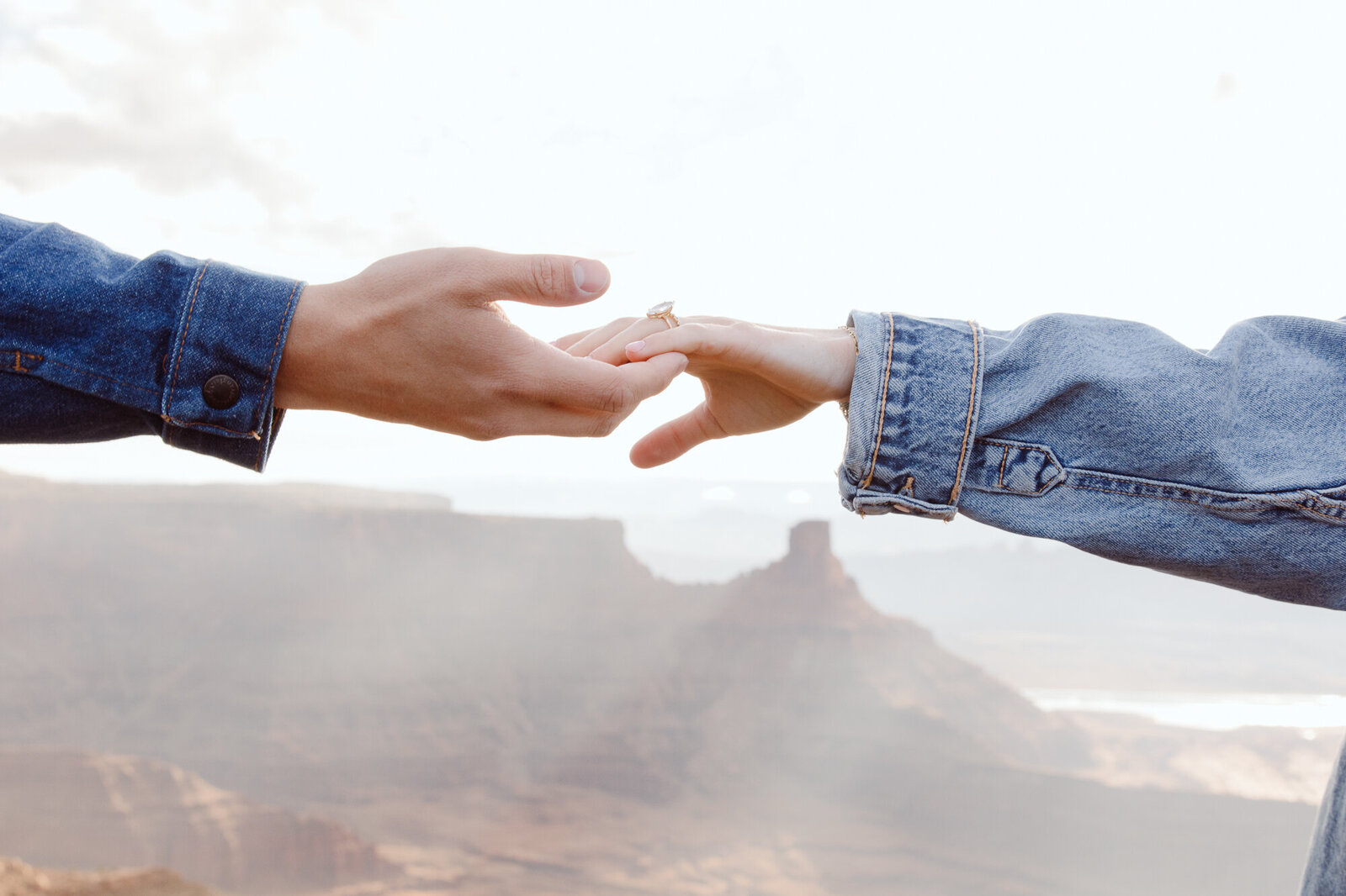 engaged couple holding each other's fingertips with a rocky landscape and lighting coming through the clouds