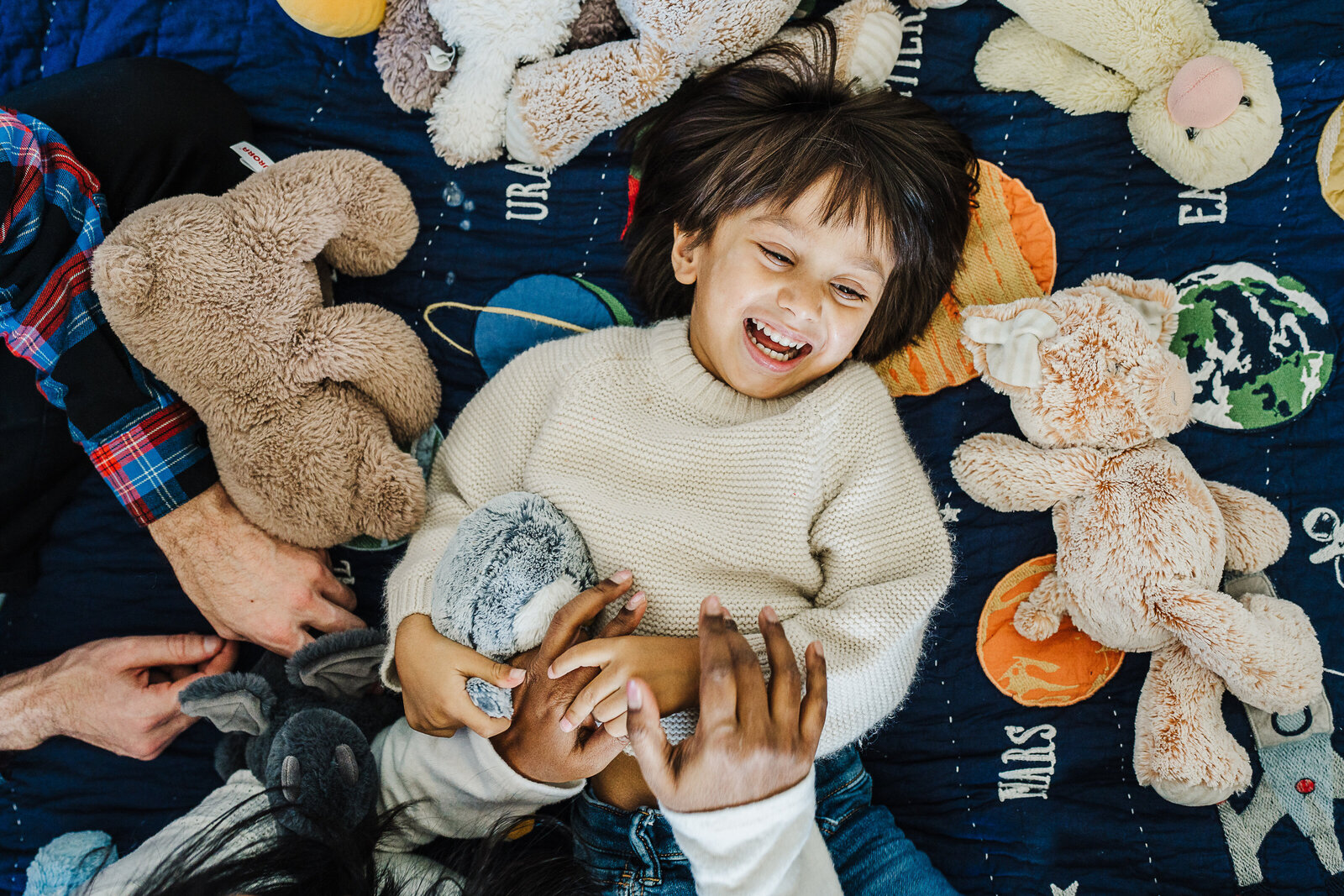 boy laughs on bed surrounded by stuffed animals