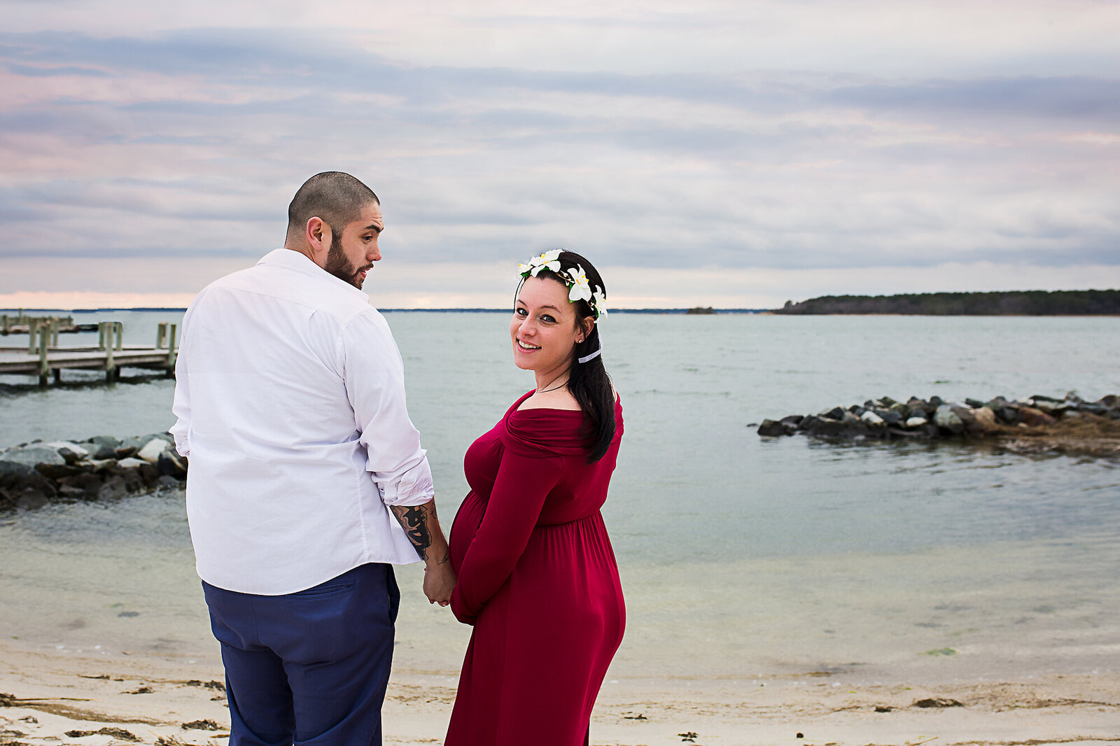 pregnant woman in red dress posing with husband on the beach
