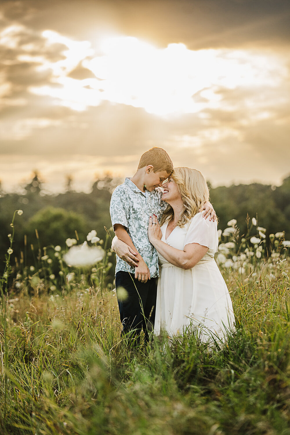 mom in white dress snuggles son in field of queen annes lace