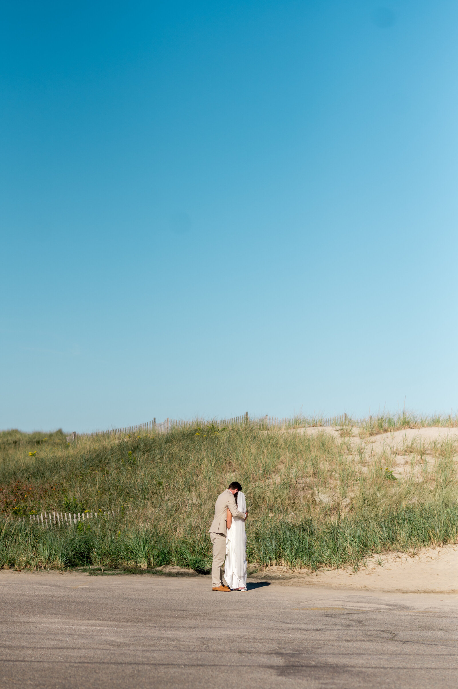 Bride and groom candidly hugging along coastal dunes during intimate Cape Cod beach wedding — natural, romantic New England photography by Sarah Surette Photography