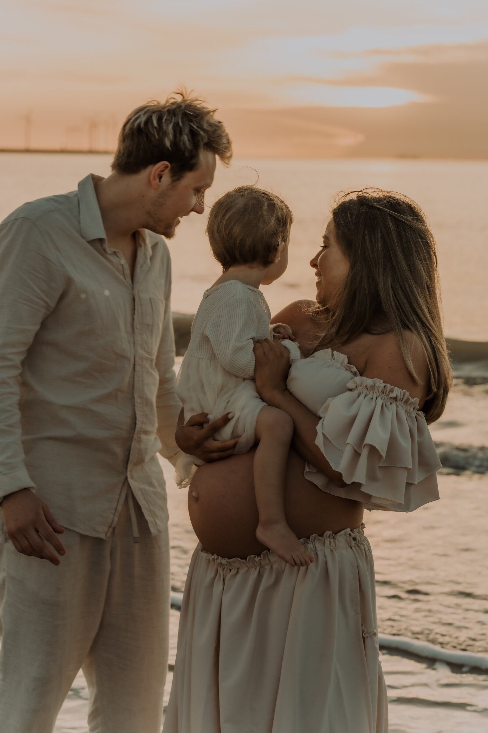 Gezin poseert voor zwangerschapsshoot op het strand tijdens zonsondergang