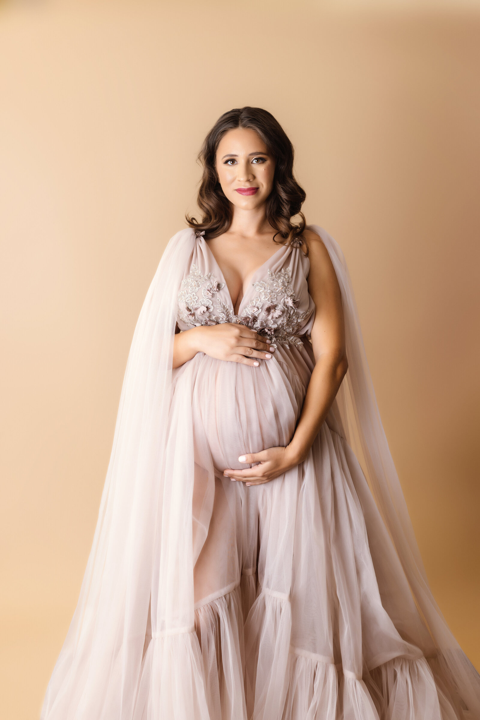Maternity Photographer, a pregnant woman holds her belly, she wears a gown
