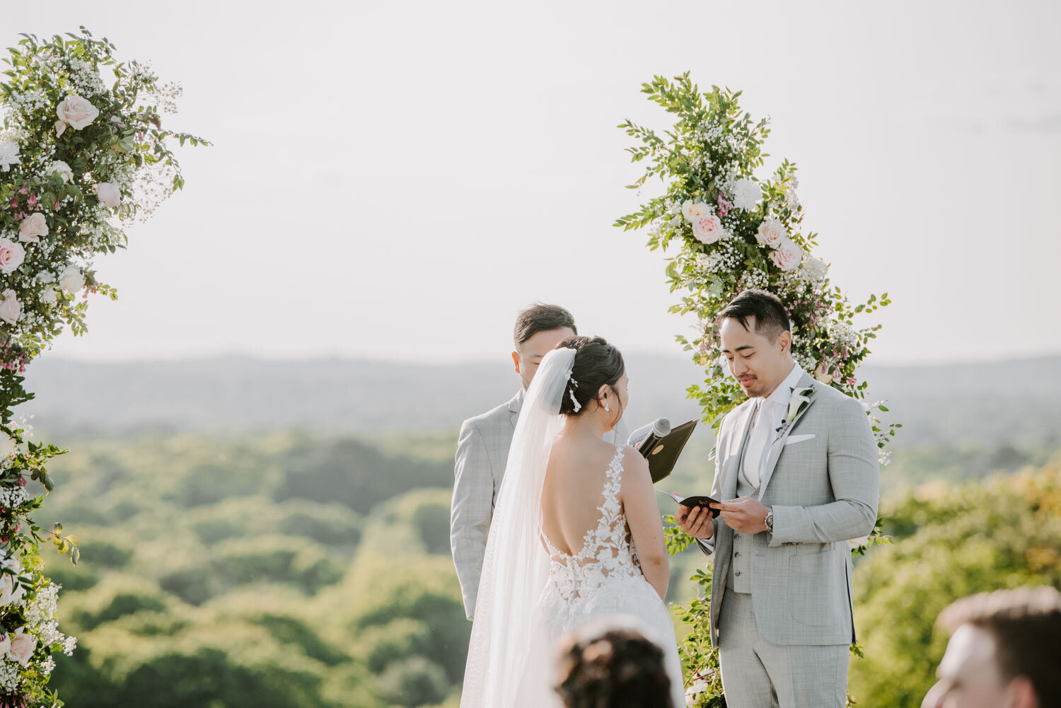 Bride and groom exchanging vows under a floral arch with scenic views