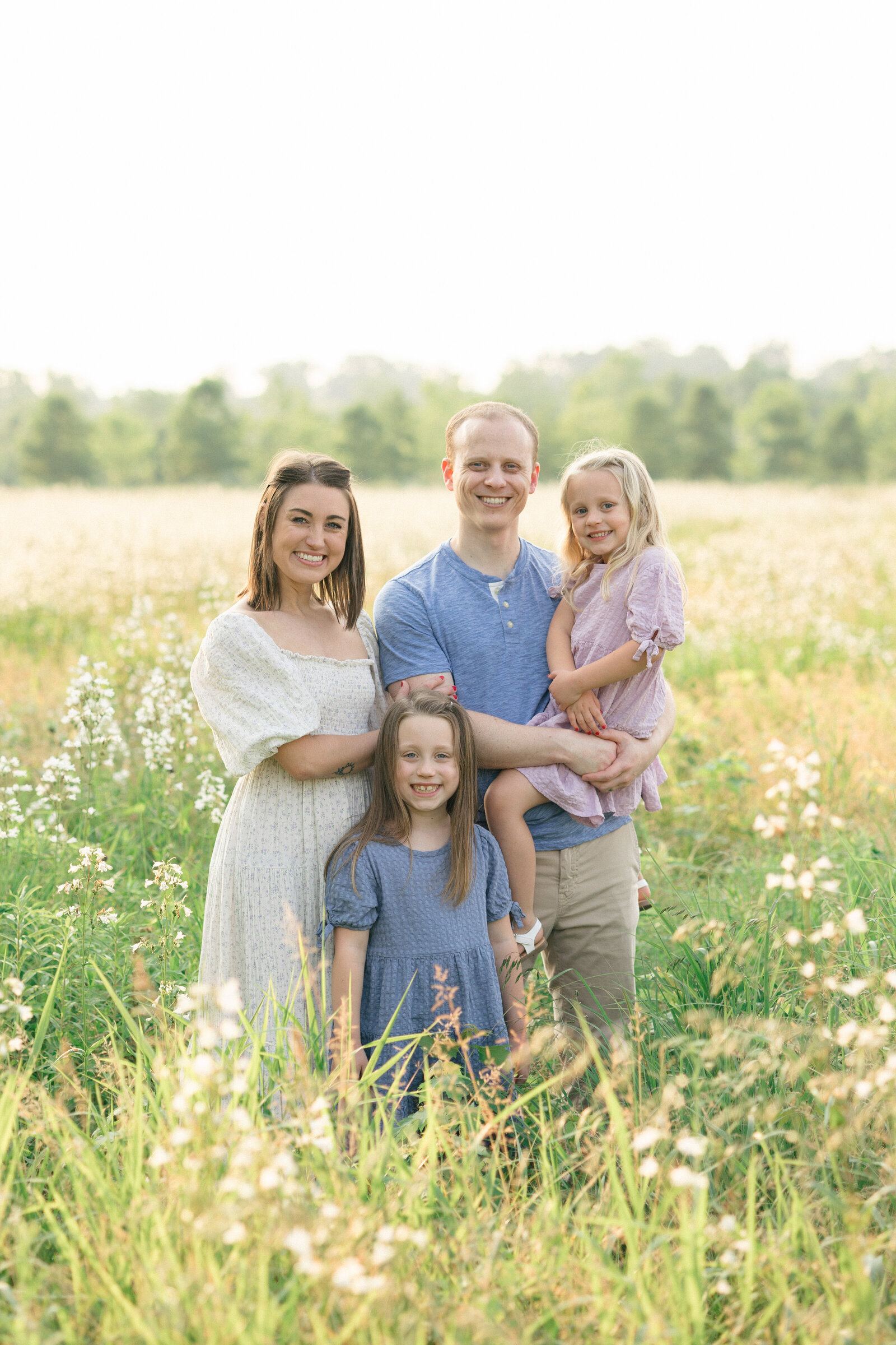 Beautiful family of four smiling in a field of white wildflowers