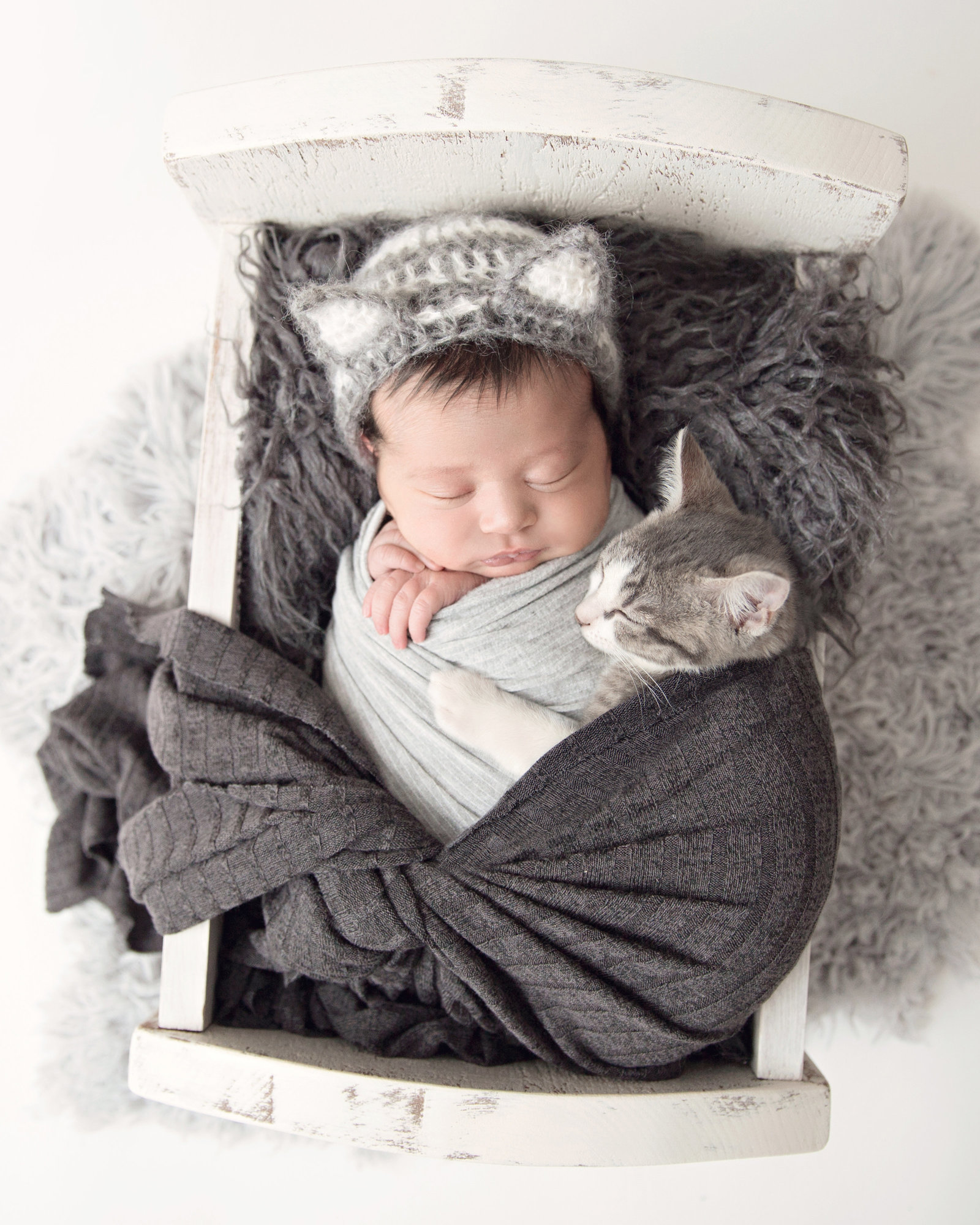 sleeping newborn baby swaddled with kitten in small wooden bed