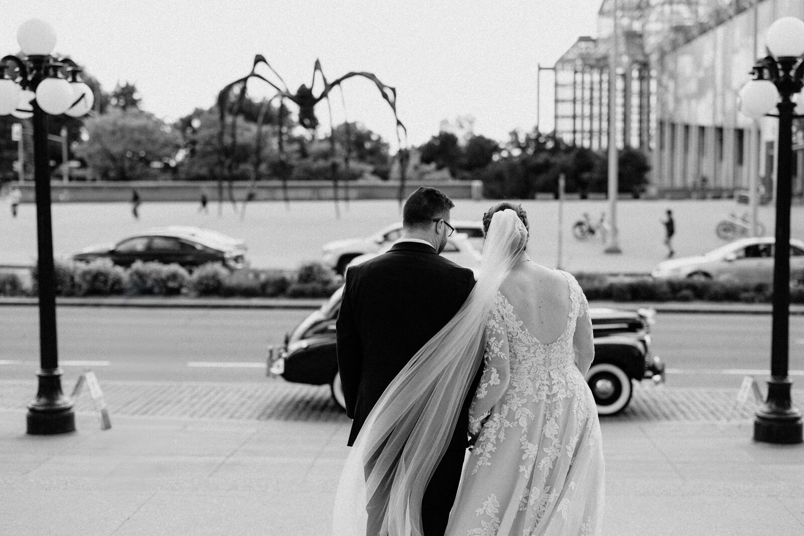 A black and white back shot of a newly wedded couple heading towards their wedding car