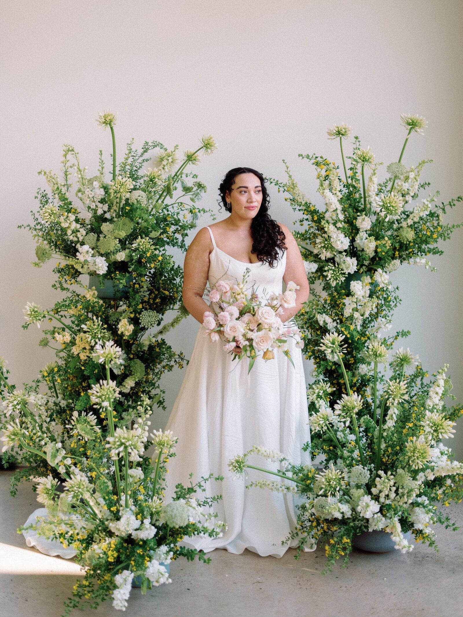A bride stands in the middle of a large floral installation cascading around her.