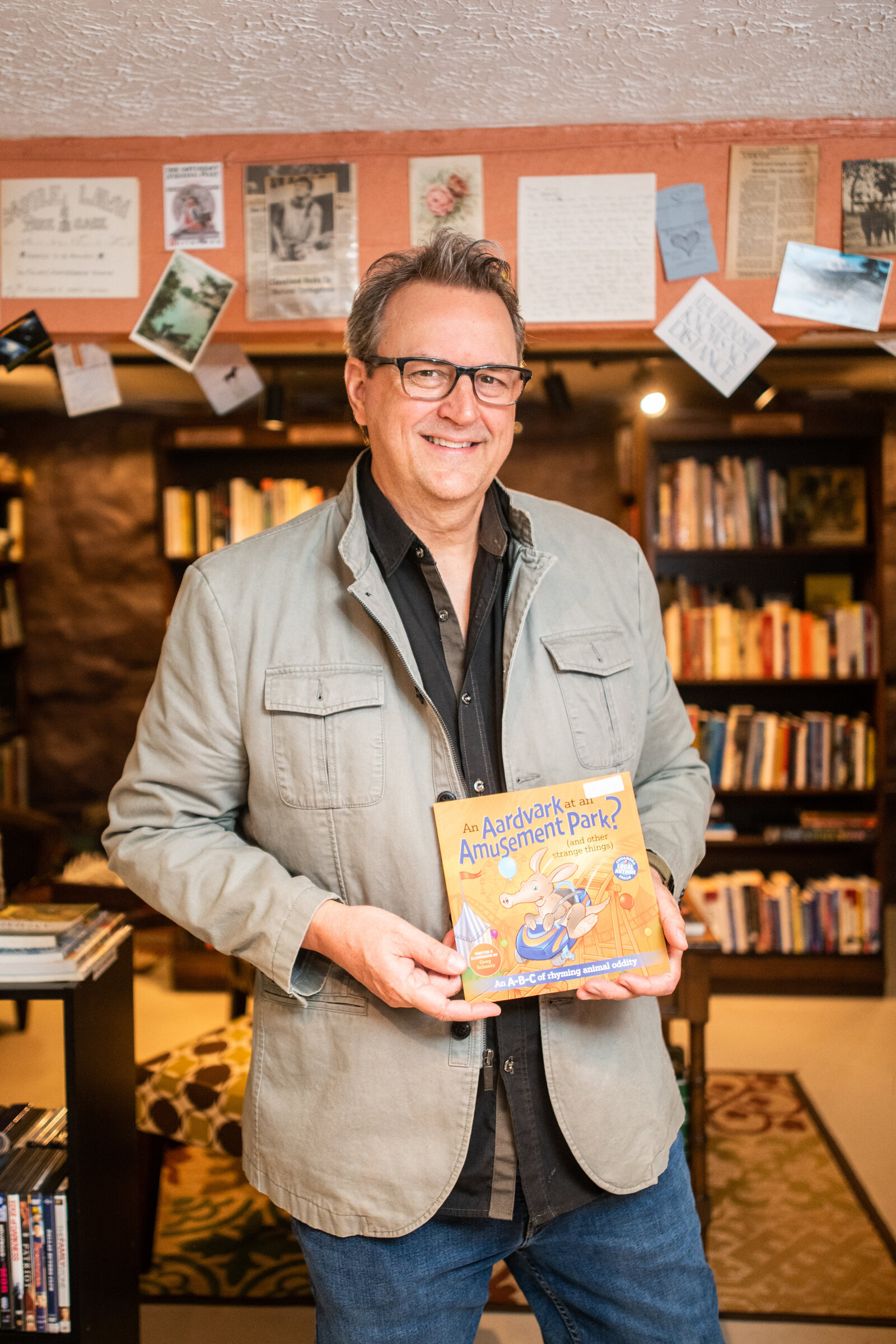 author holds his book in front of bookshelves at shelf life bookstore