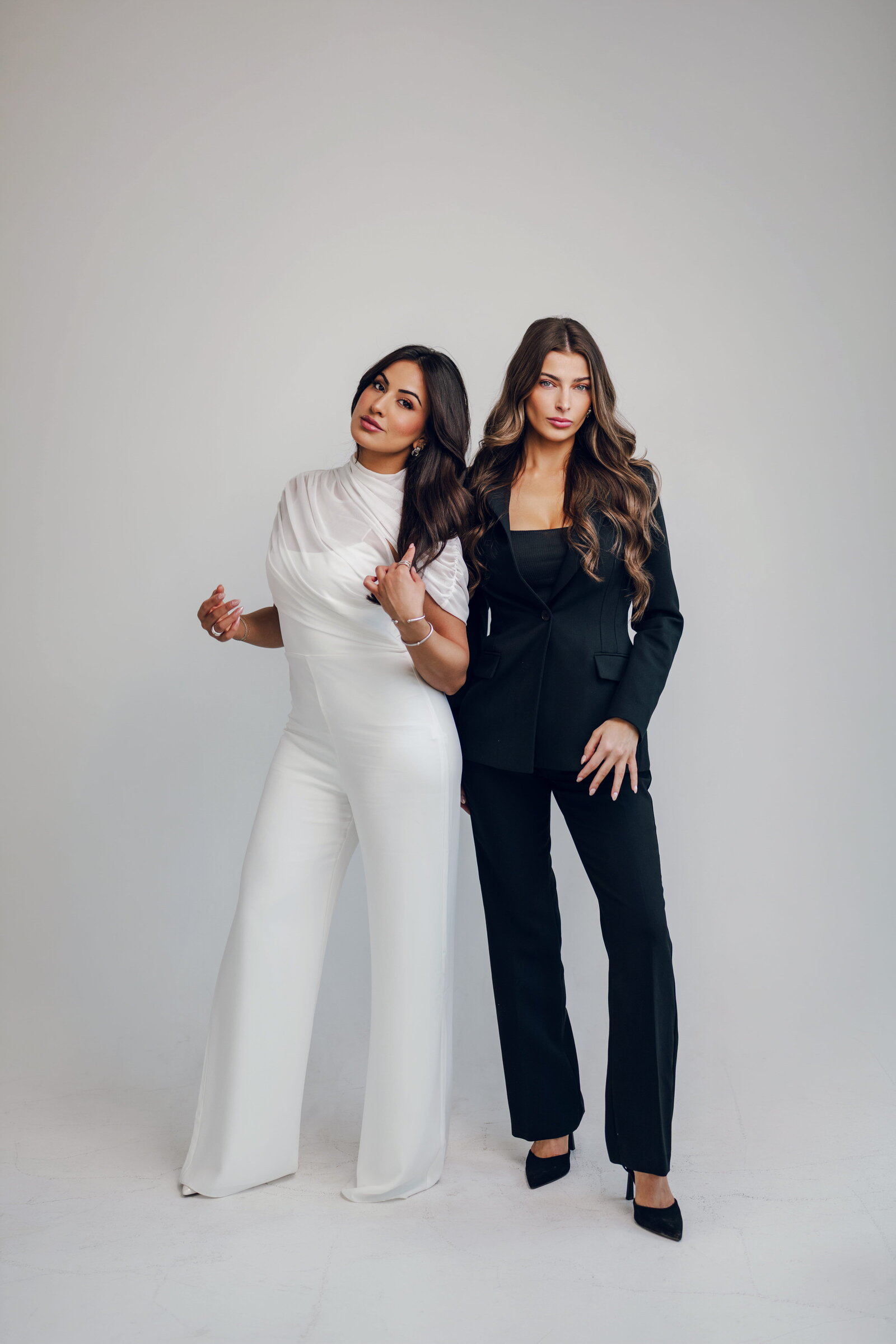 Two women in a white suit and a black suit posing in a studio