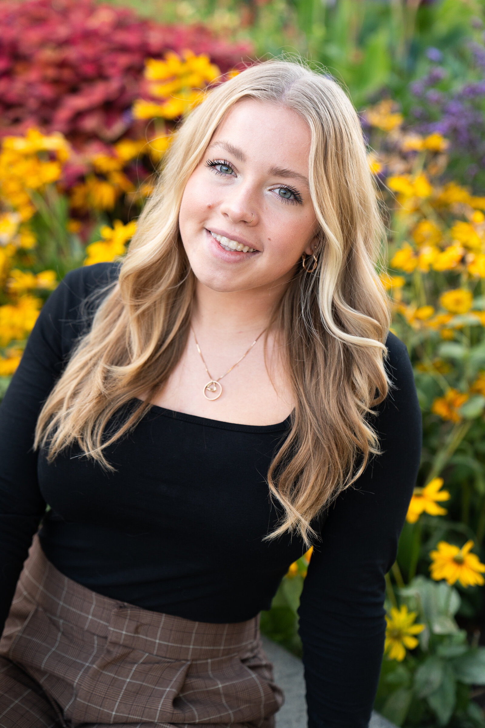 Girl sits by fall colored flowers during her senior picture session at the Minnesota Landscape Arboretum in Chaska, Minnesota.