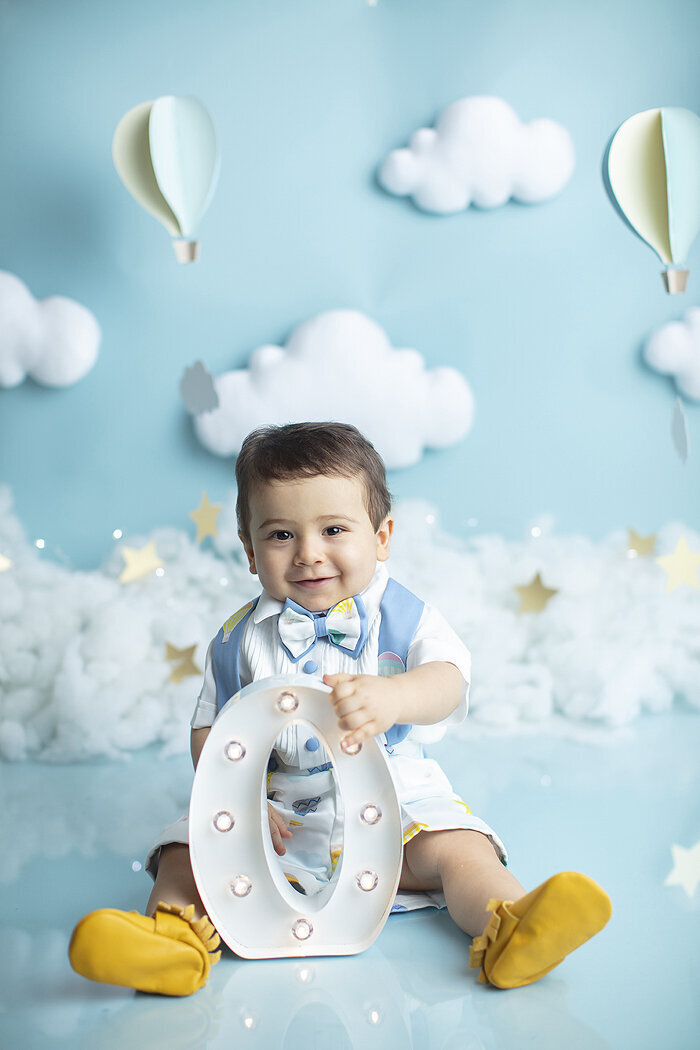 Baby boy holding letter O at his first birthday photoshoot.